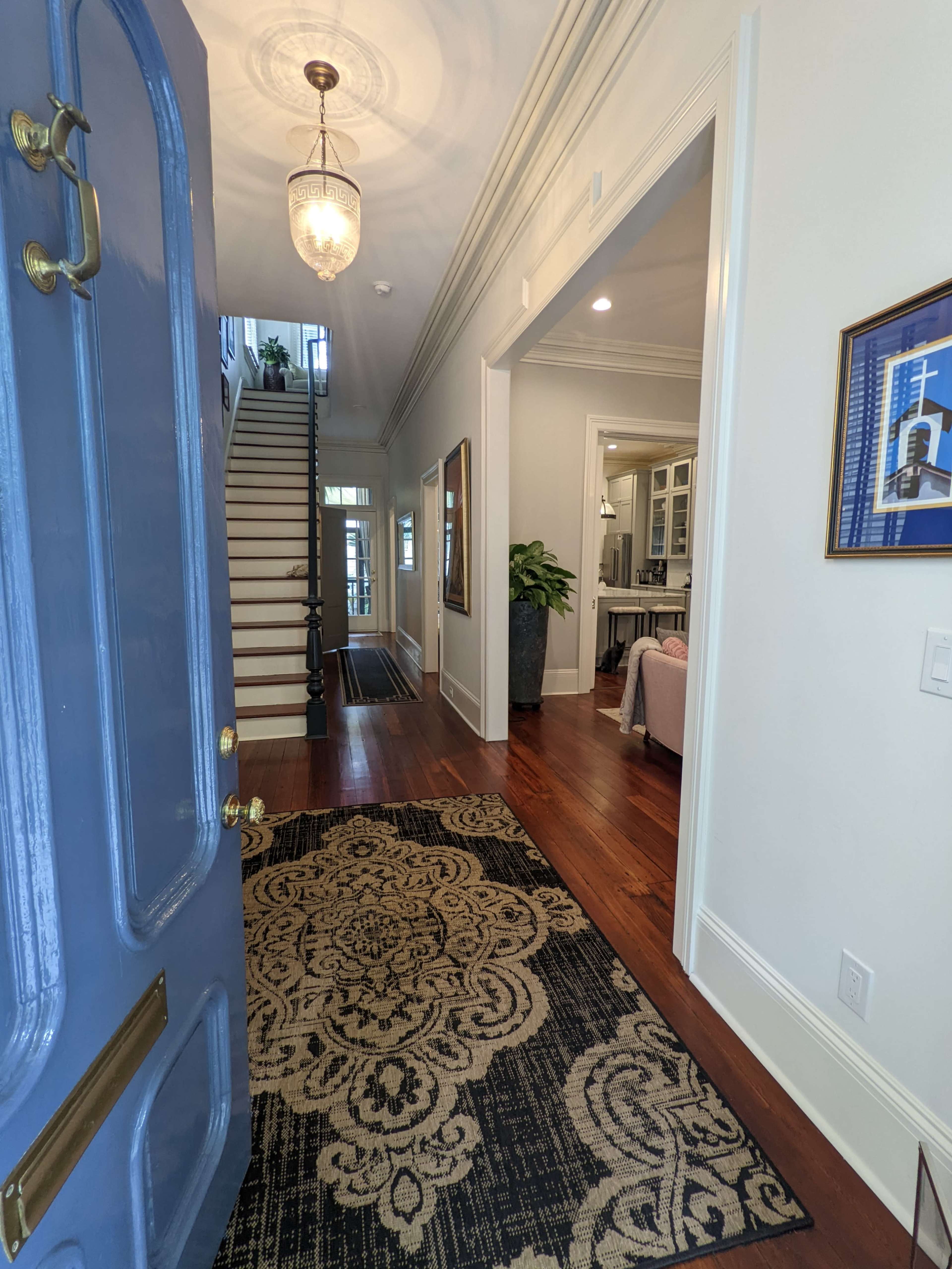 A front door opens to a hallway featuring a staircase, a decorative rug, and doorways leading to adjacent rooms.