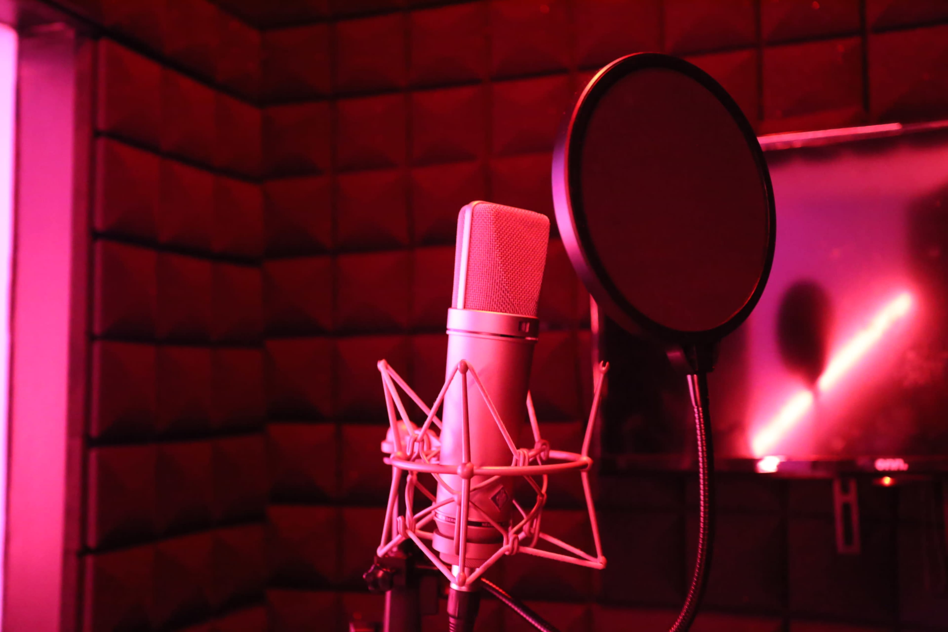 The image shows a microphone with a pop filter set against a backdrop of red-lit acoustic foam panels.
