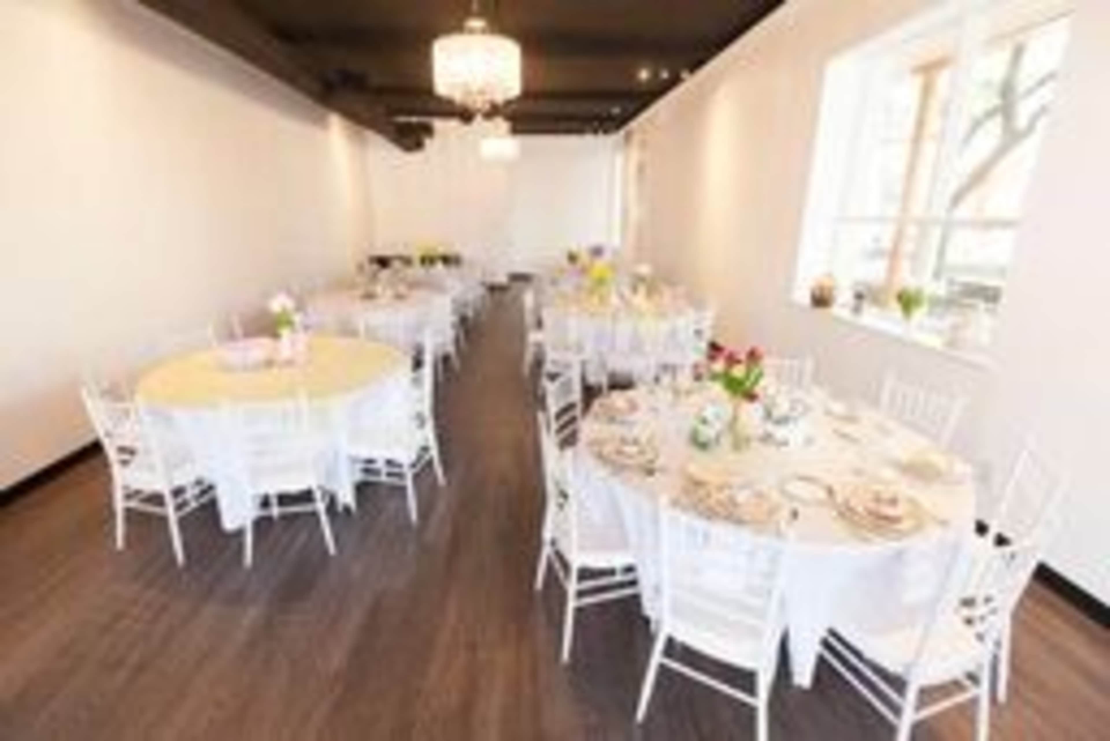 A spacious event room set with round tables covered in white tablecloths and adorned with floral centerpieces.