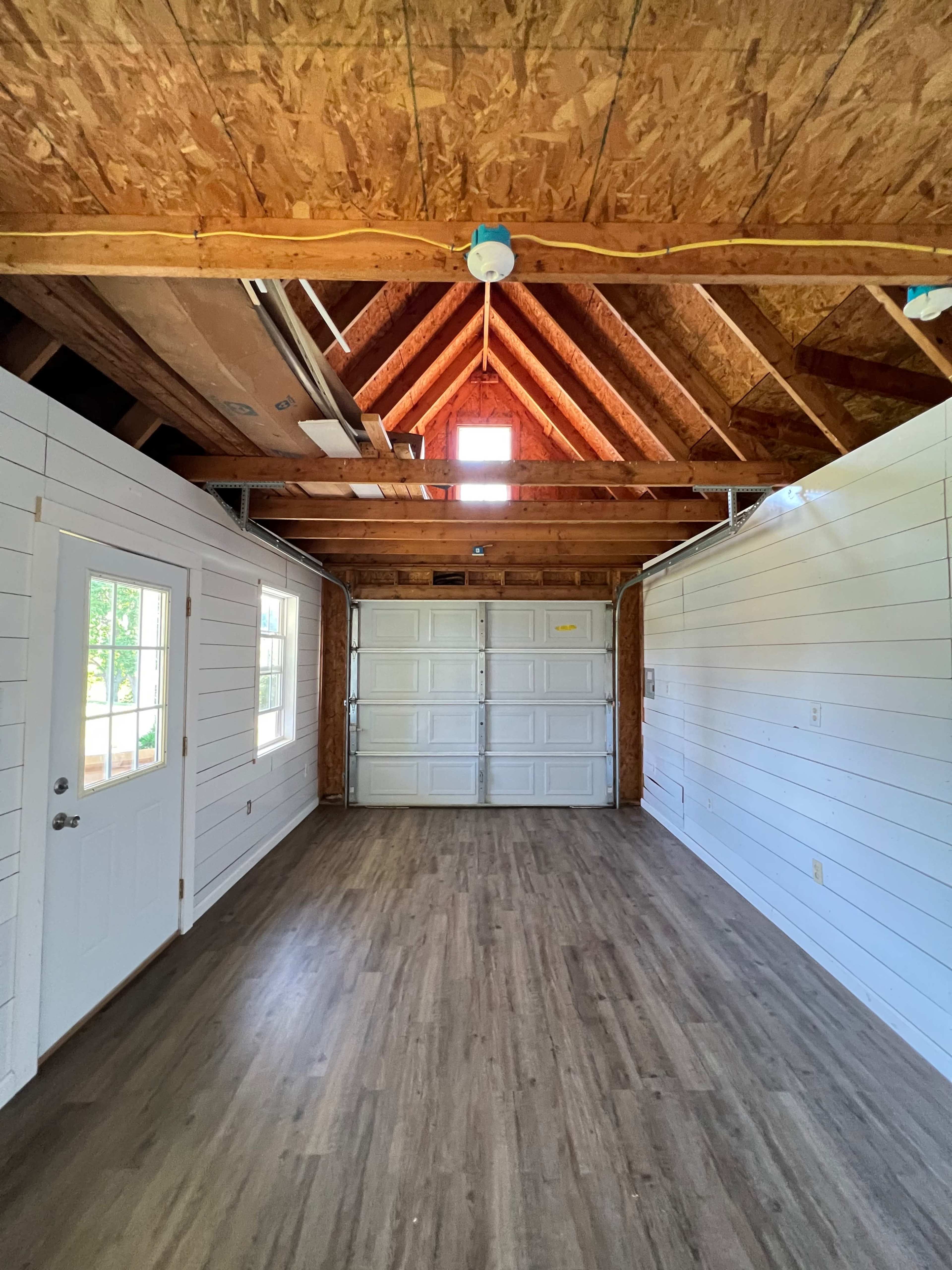 The image shows the interior of a spacious garage with a vaulted ceiling, wooden beams, and two garage doors at one end.