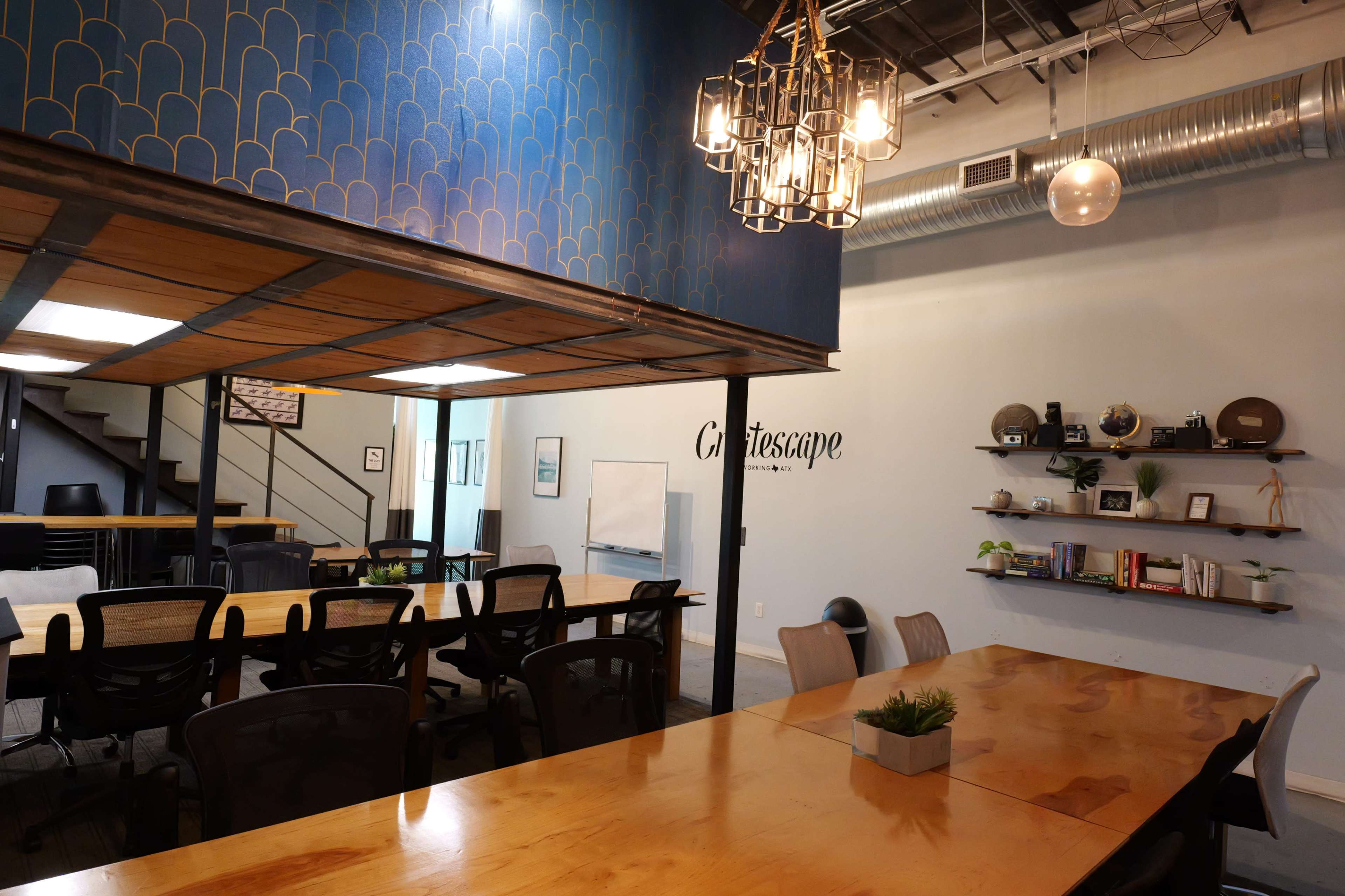 The image shows a modern conference room with a large wooden table, black chairs, a blue accent wall, and a staircase leading to an upper level.