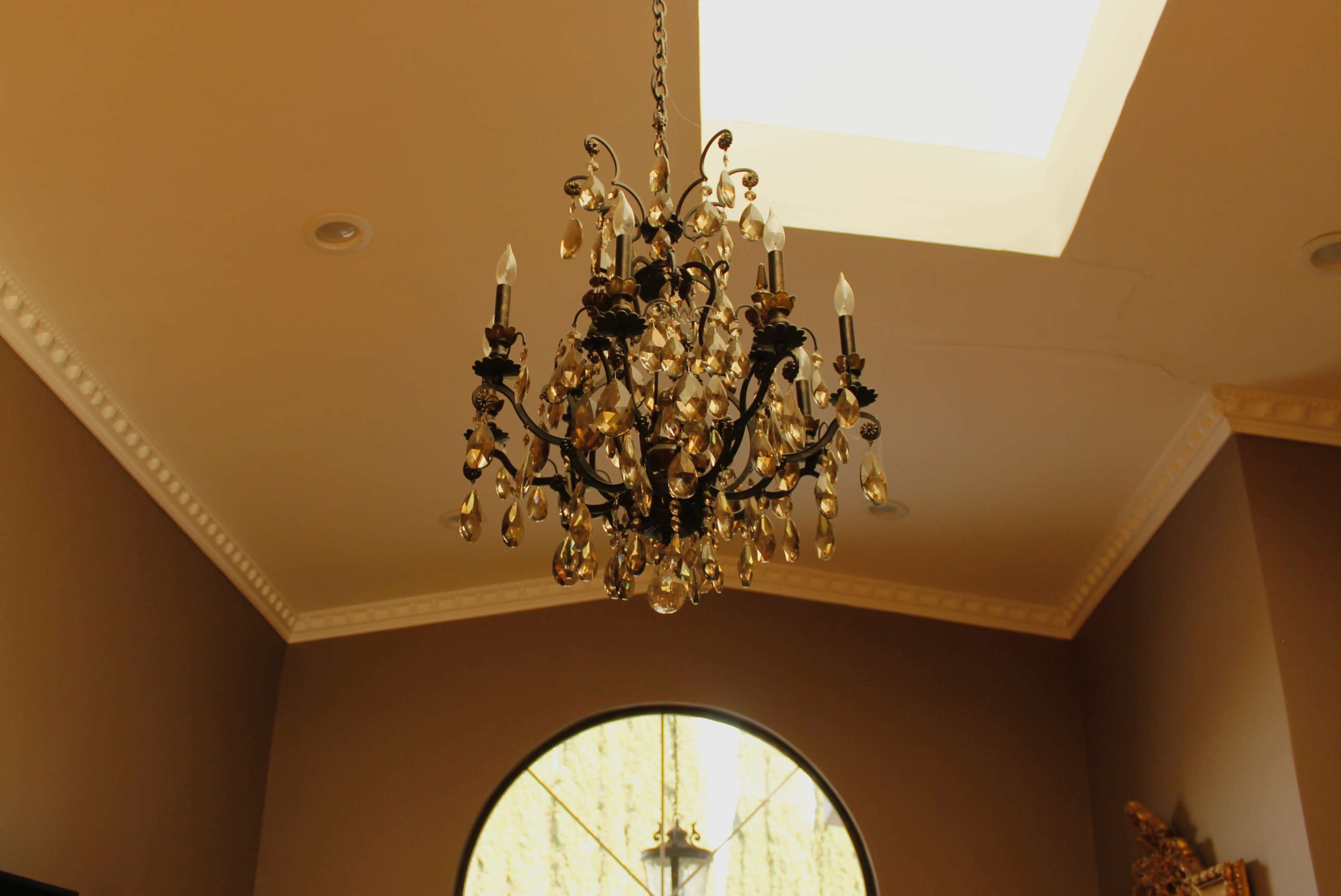 A decorative chandelier hangs from the ceiling beneath a skylight in a room with a rounded window.