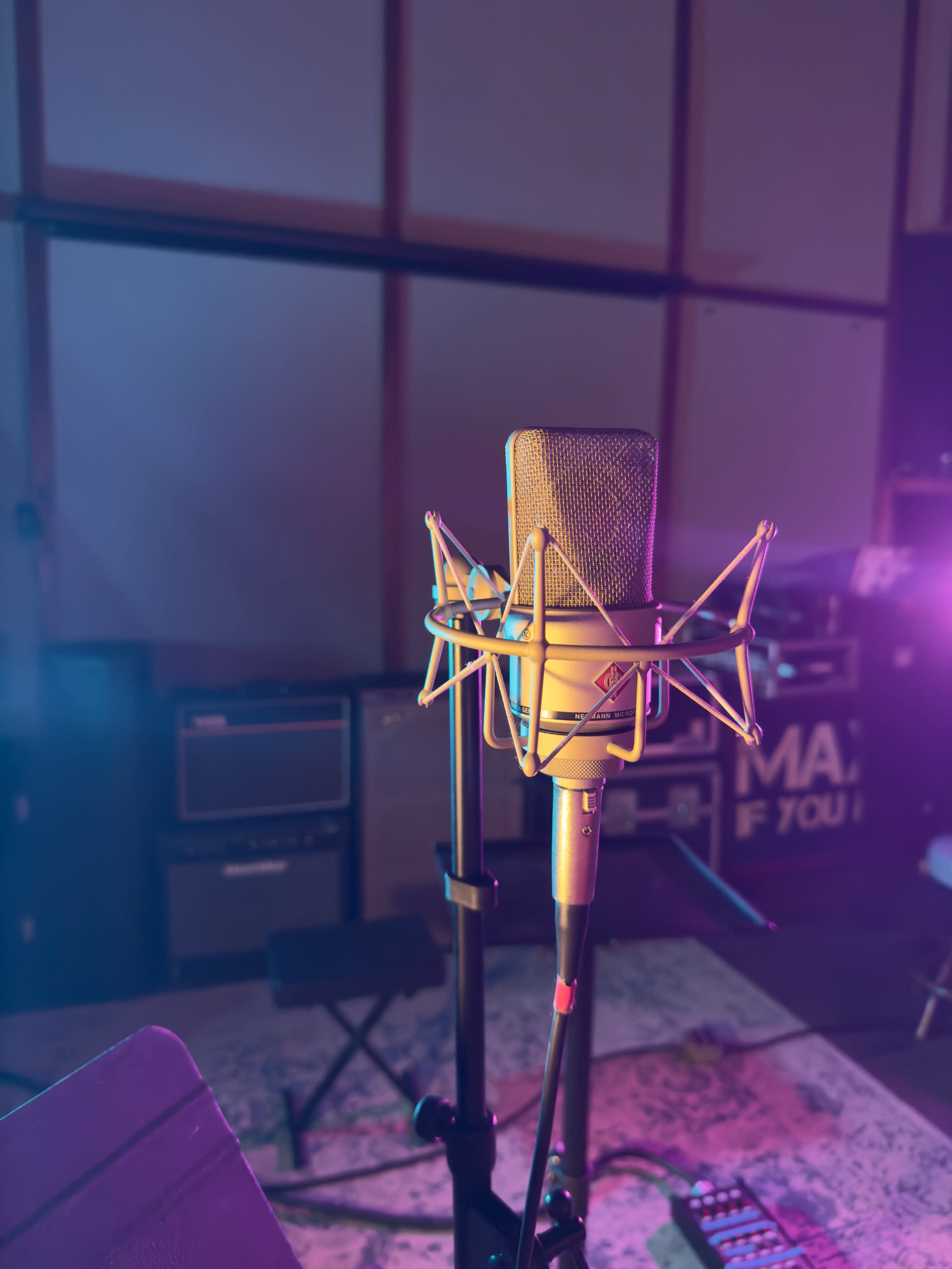 A professional microphone is positioned on a stand in a dimly lit recording studio, surrounded by colorful lighting and music gear.