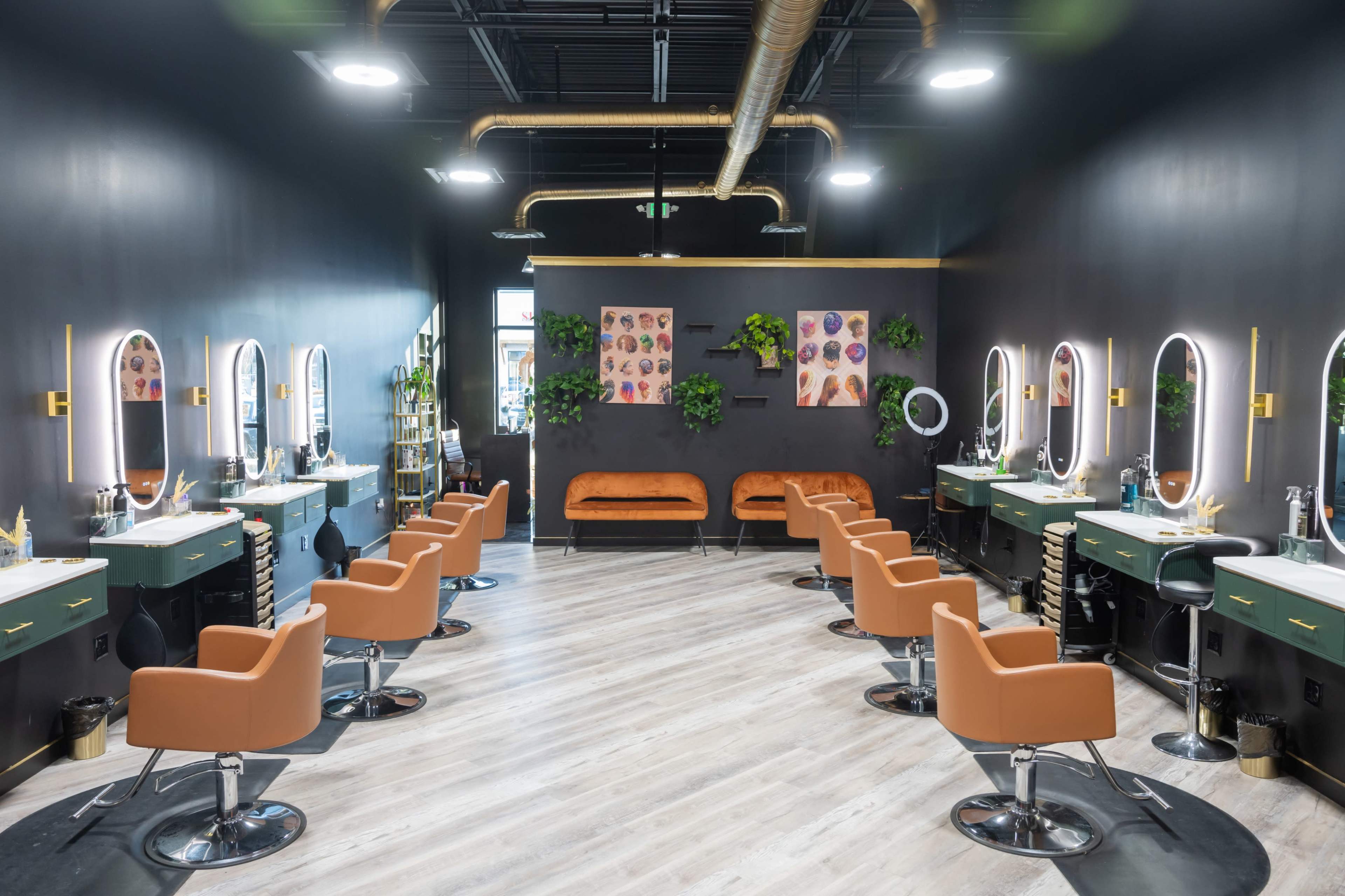 A hair salon features eight styling stations with circular mirrors and orange chairs, set against black walls and complemented by green plants and artwork.