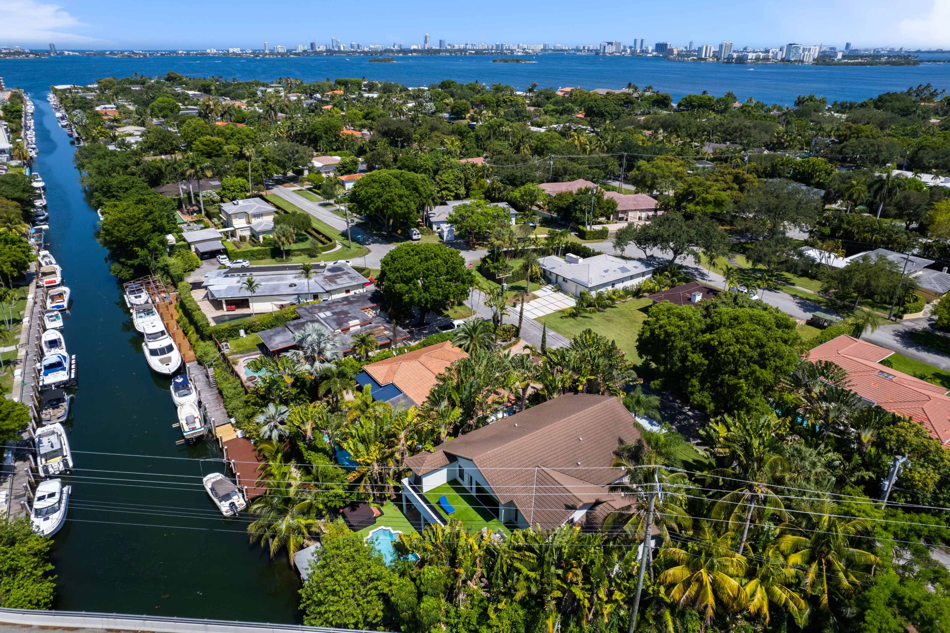 A coastal neighborhood with homes and boats lining a canal, set against a backdrop of a city skyline and blue water.