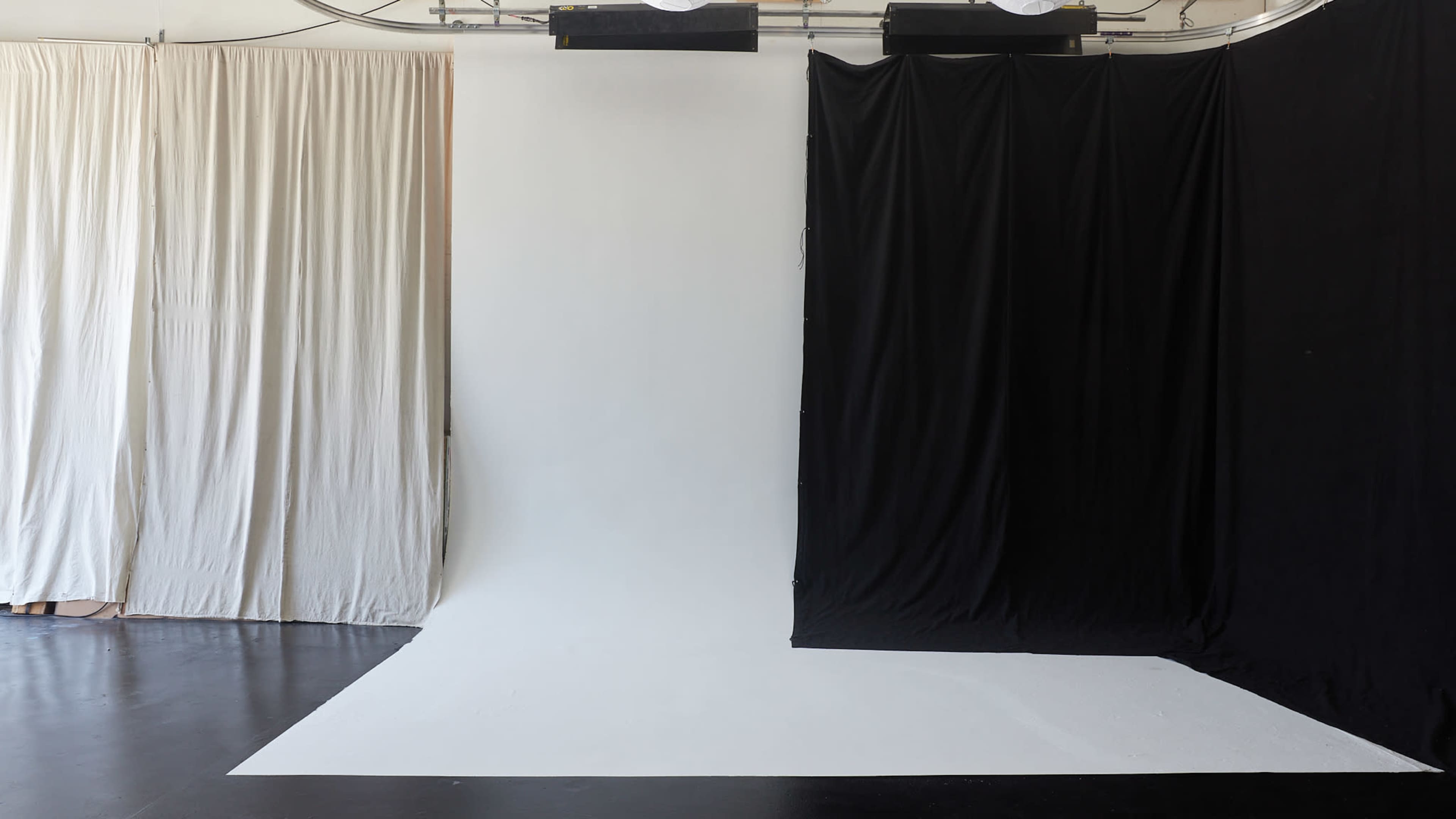 The image shows a photography studio with a white backdrop surrounded by beige and black draped fabric on the sides.