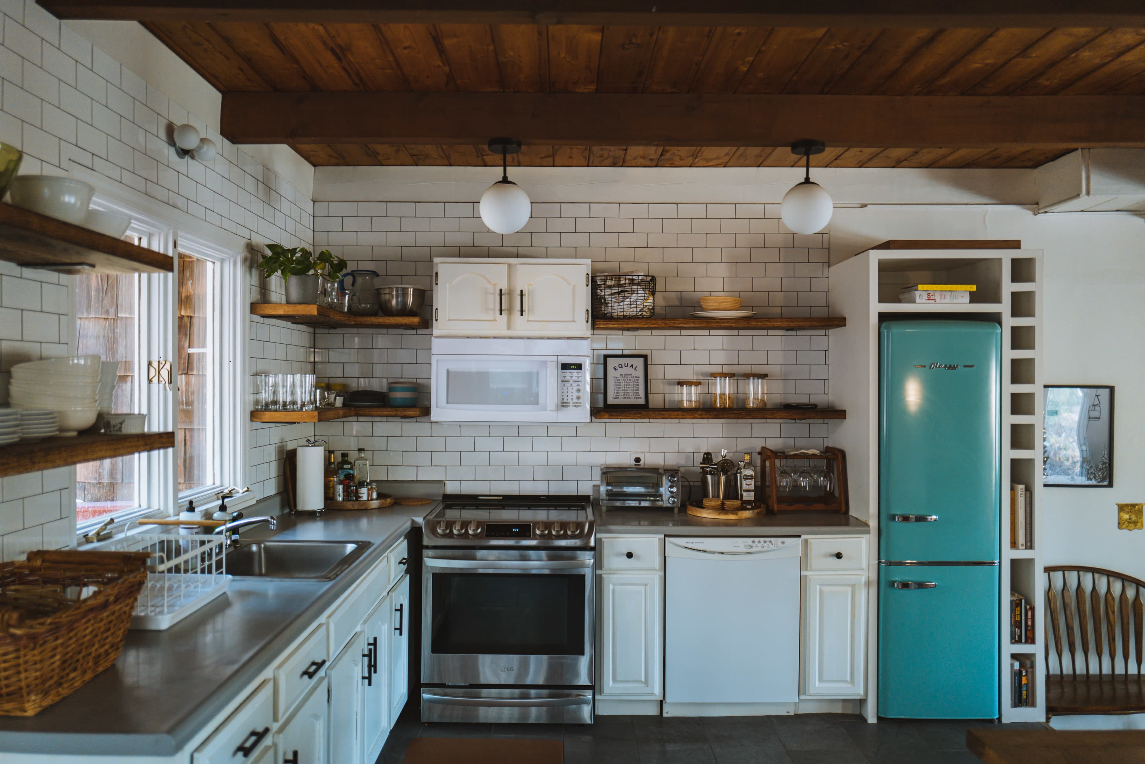A modern kitchen with white cabinets, open shelves displaying dishes, and a turquoise refrigerator.