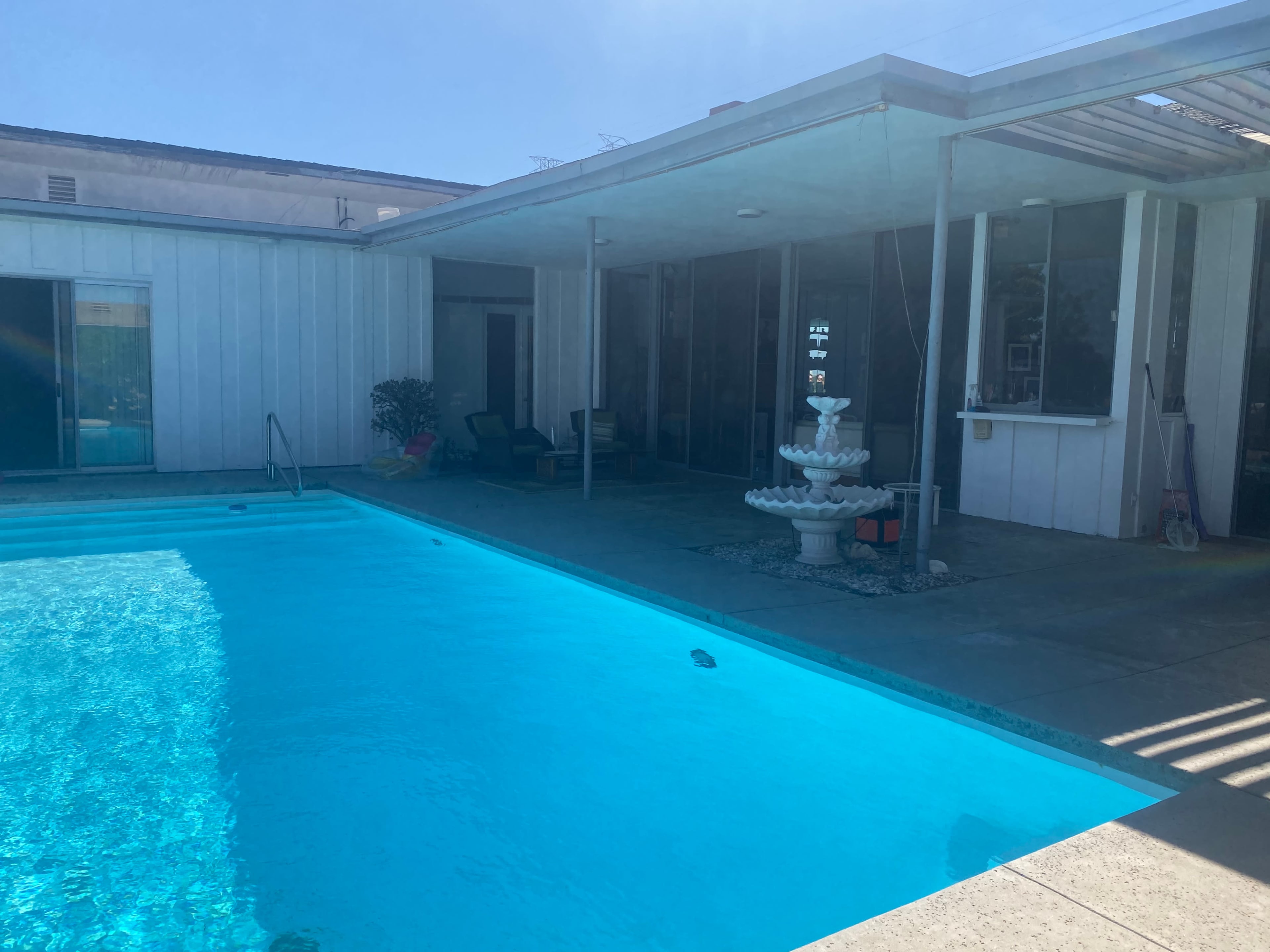 A swimming pool beside a modern house featuring a fountain and a patio area with seating.