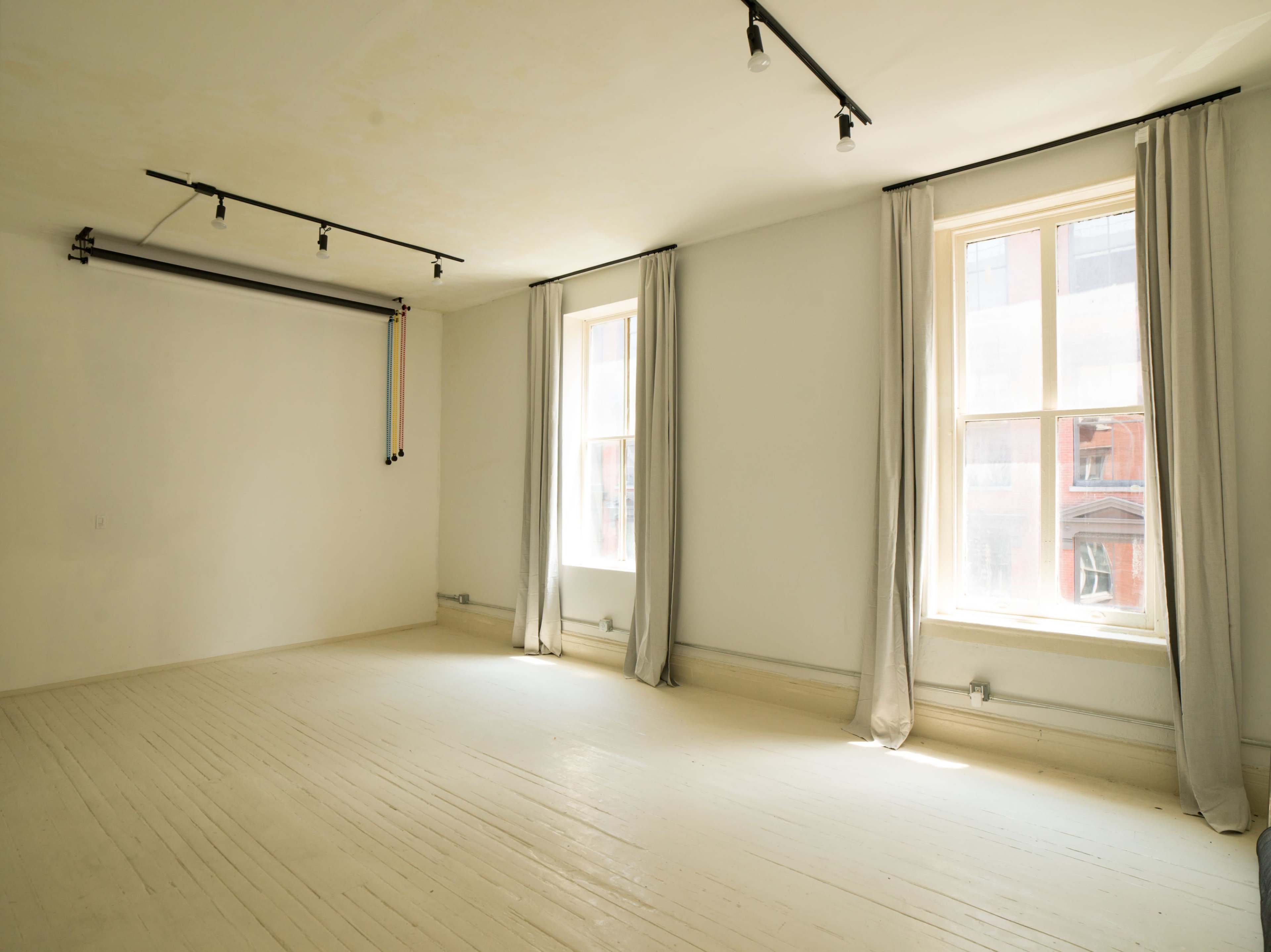 A bright, empty room with two large windows and light gray curtains on either side.