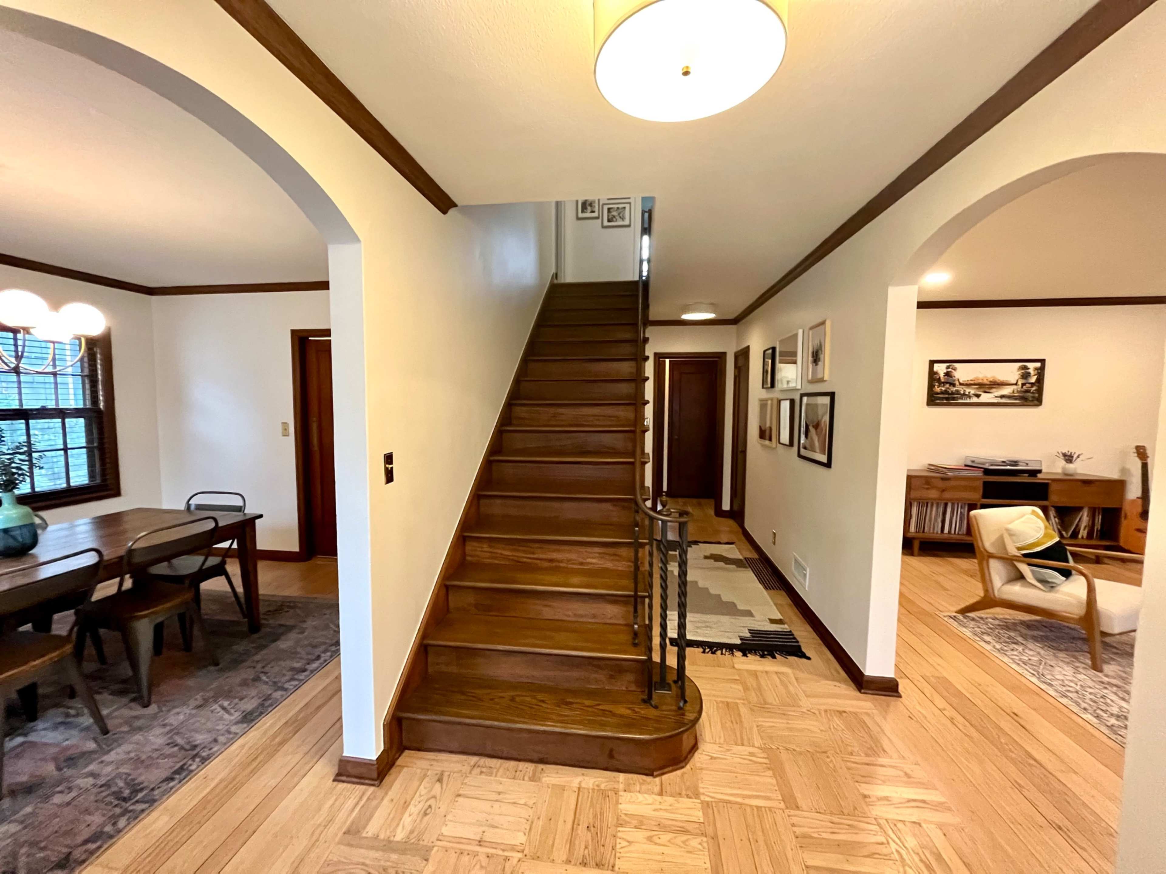 A hallway with a staircase leading to the upper floor, flanked by a dining area on the left and a living space on the right.