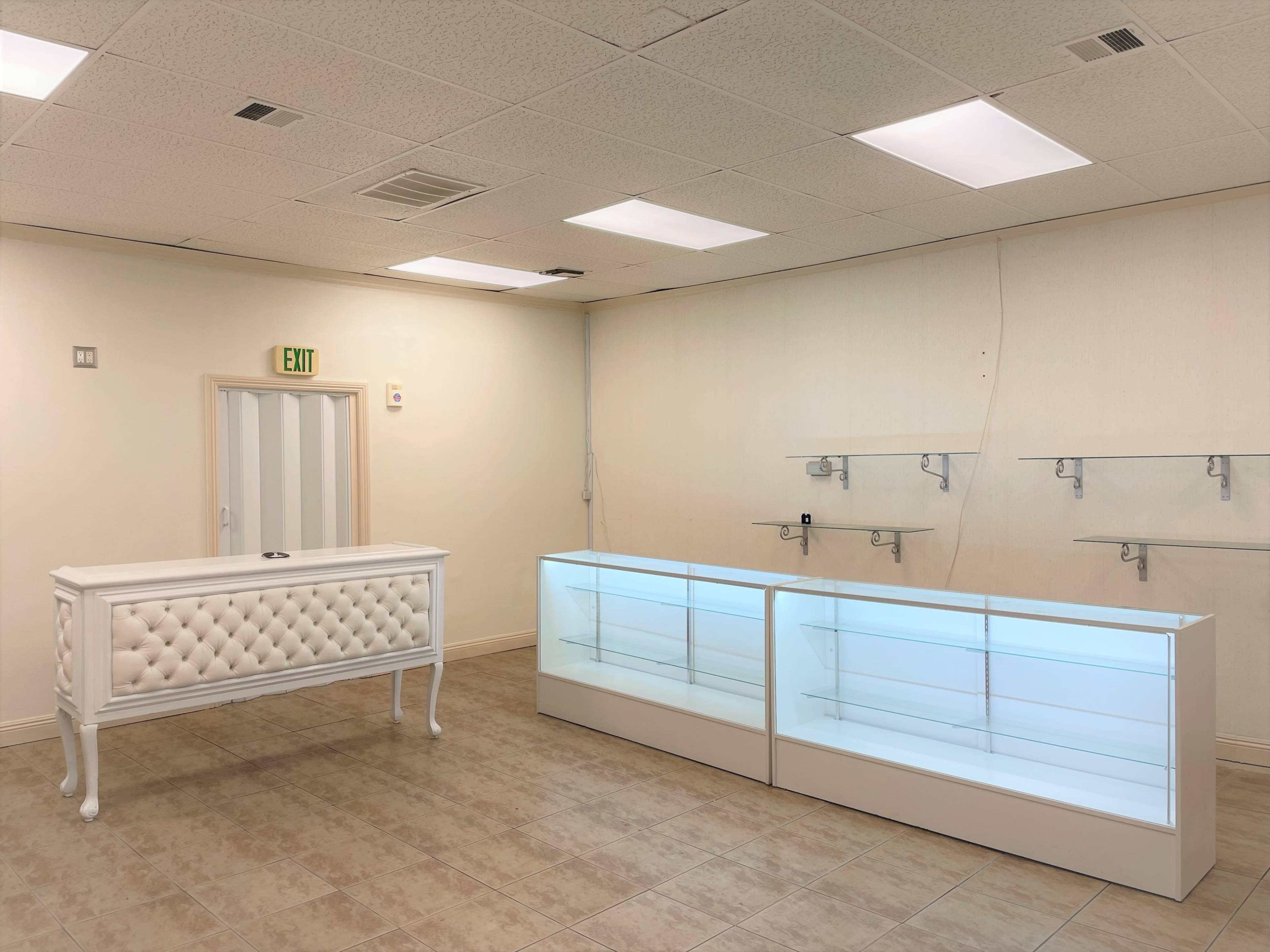 A nearly empty retail space featuring a white tufted reception desk and two illuminated display cases against a plain wall.