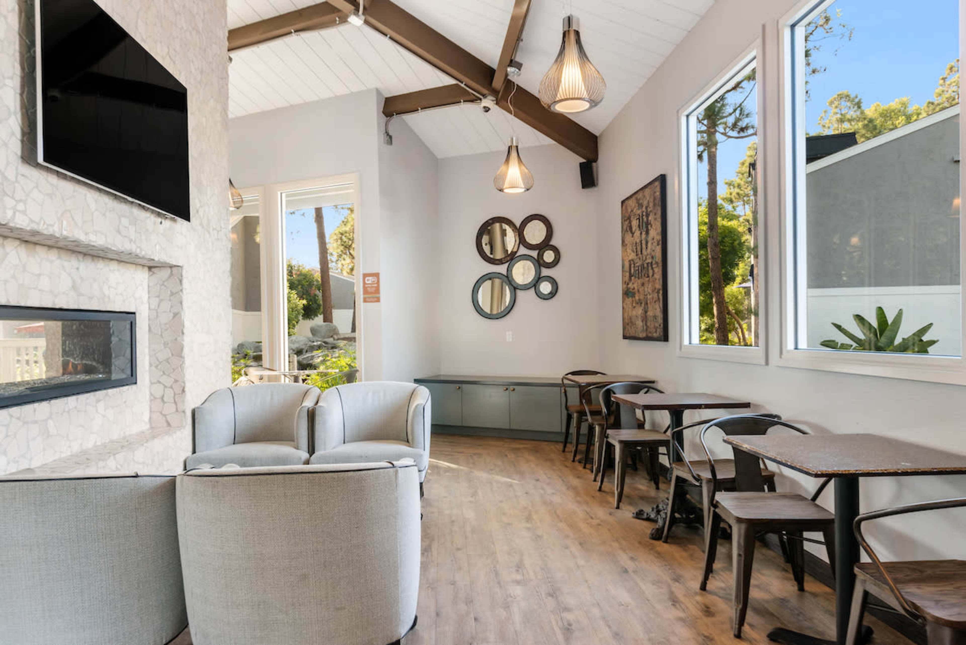 A modern café interior with two armchairs, a fireplace, multiple mirrors on the wall, and several tables and chairs arranged for seating.