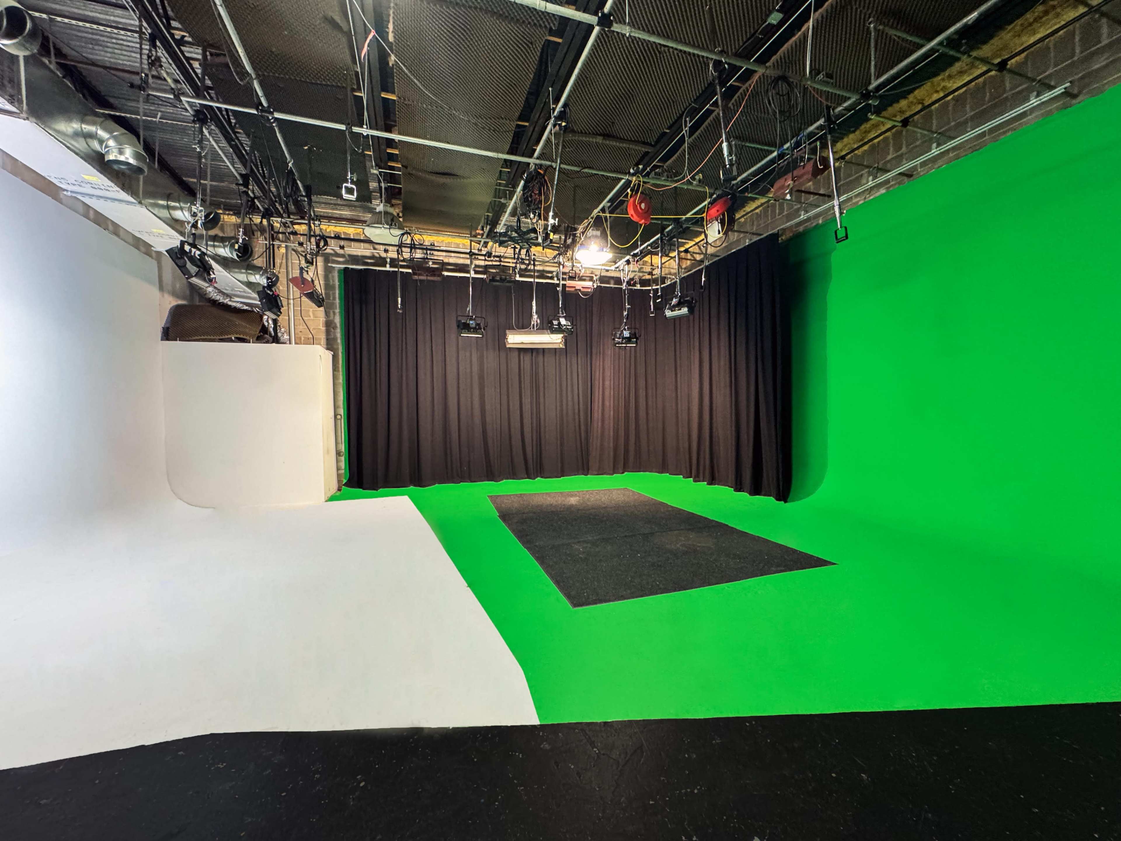 The image shows a studio space divided into areas with a green screen, a white backdrop, and a dark carpeted section.