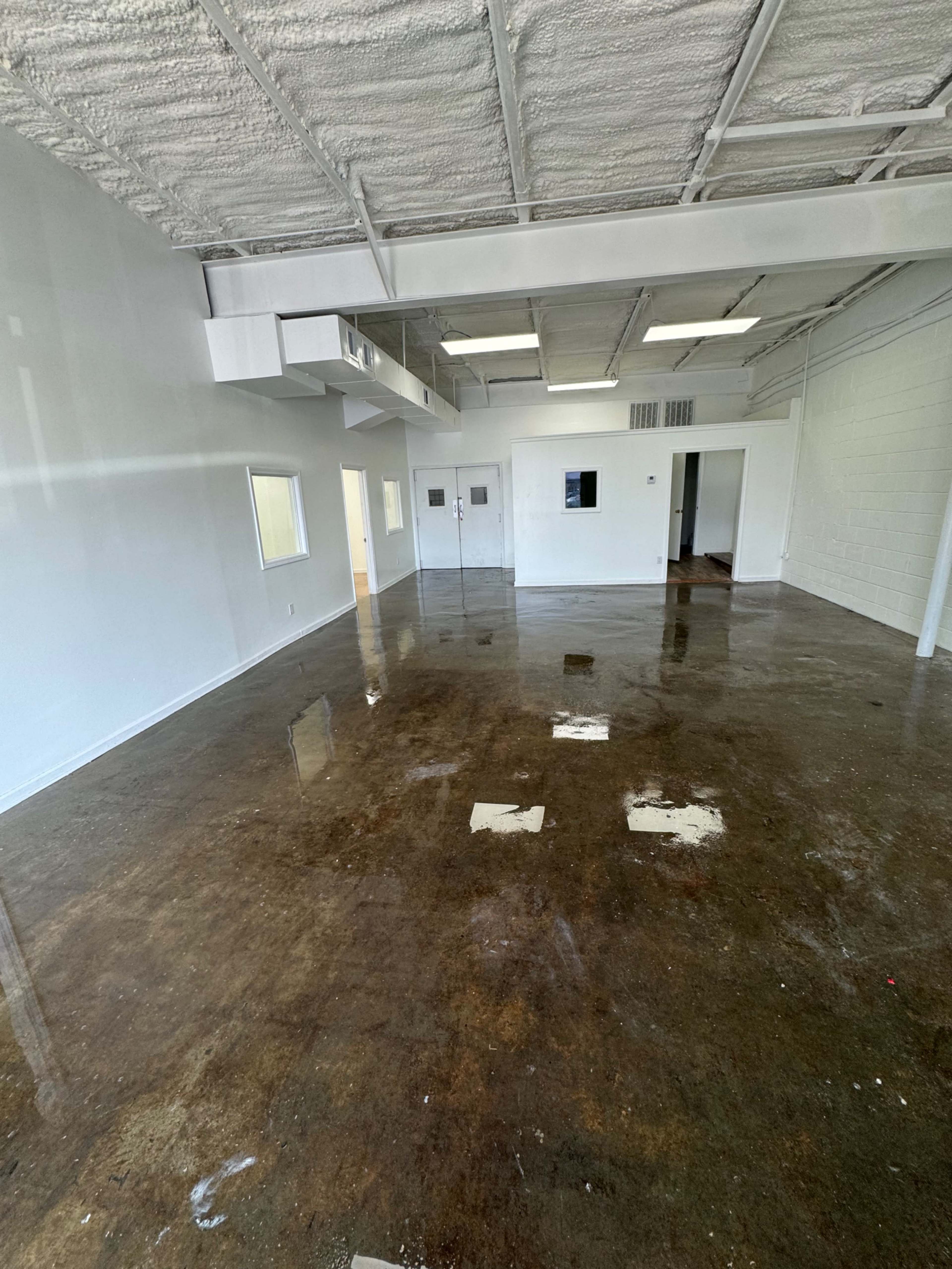 The image shows an empty office space with a polished concrete floor and white walls, featuring several doorways and windows.
