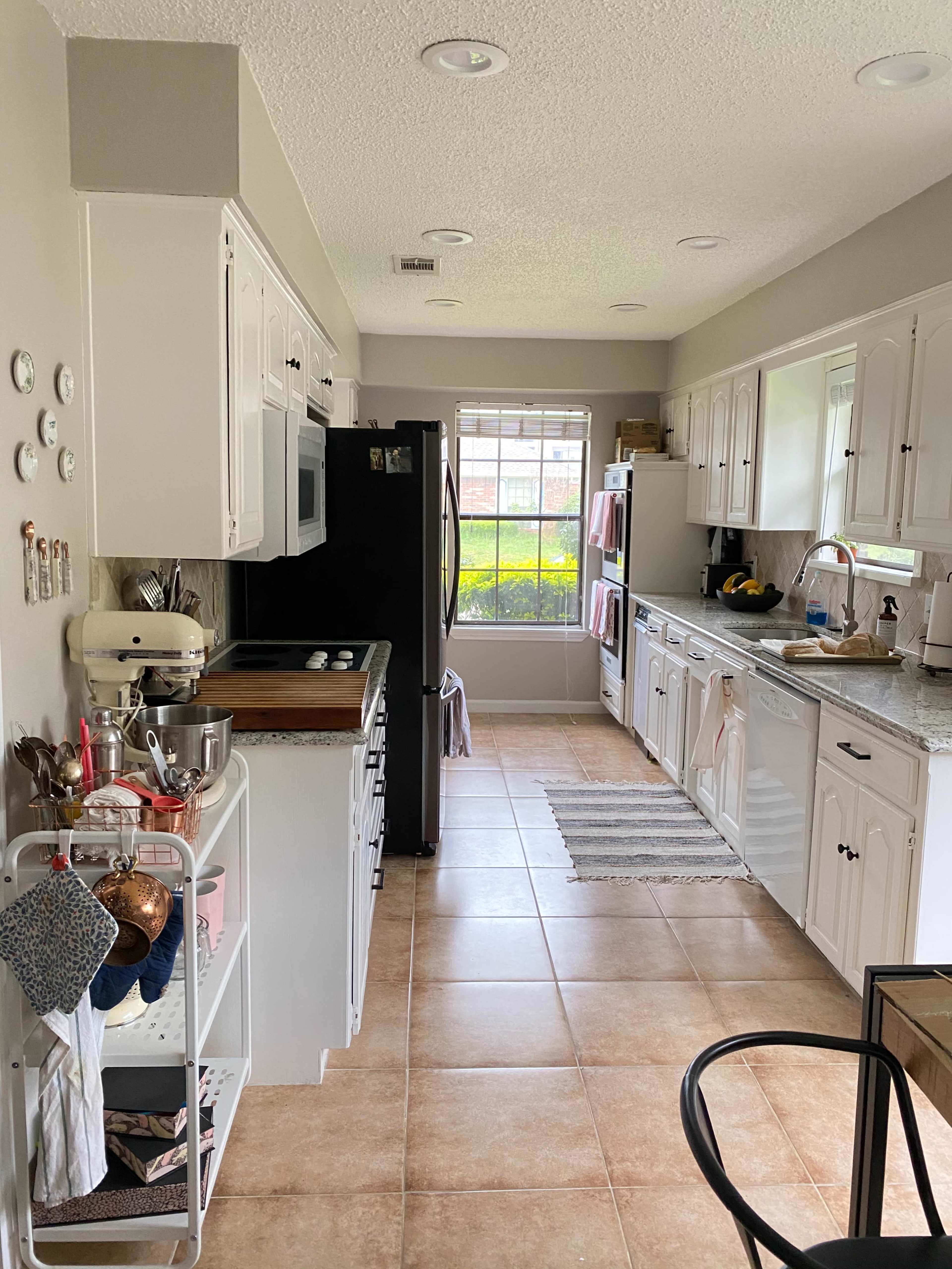 A tidy kitchen features white cabinets, a black refrigerator, and a window overlooking a green outdoor space.