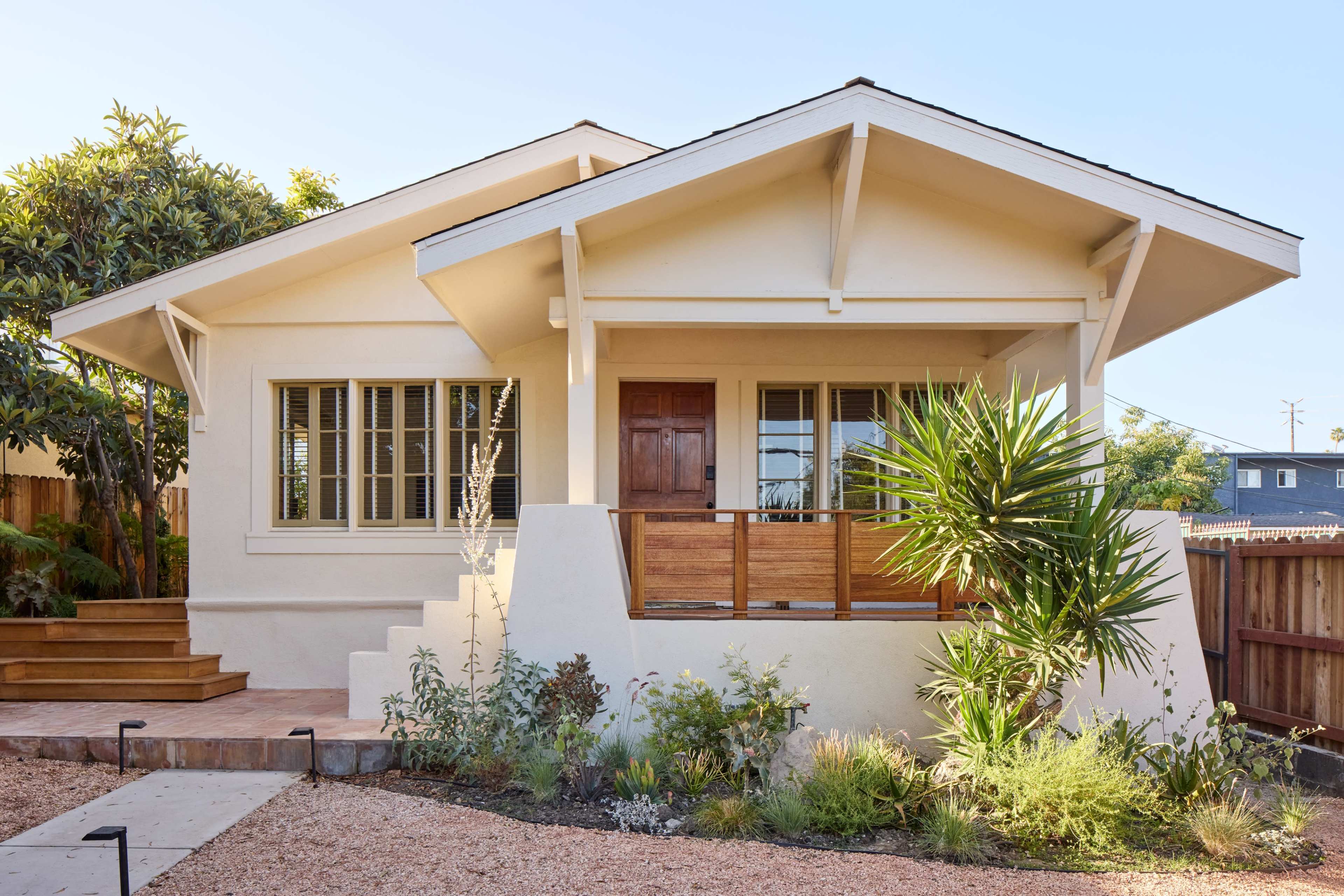The image shows a single-story house with a front porch, surrounded by landscaped gardens and a wooden railing.