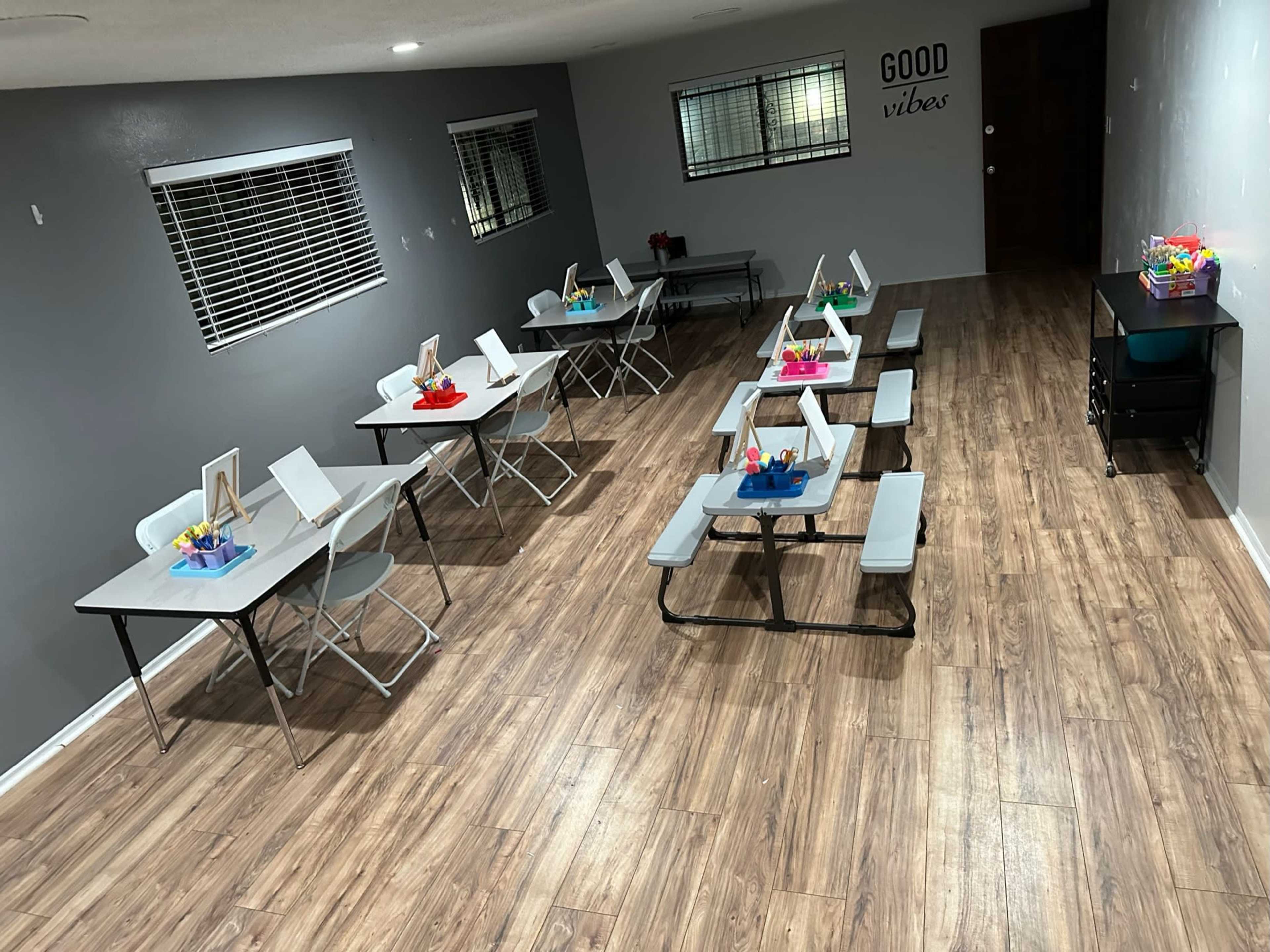 A spacious room with several tables arranged in rows, each featuring colorful centerpieces, along with a small storage unit against the wall.