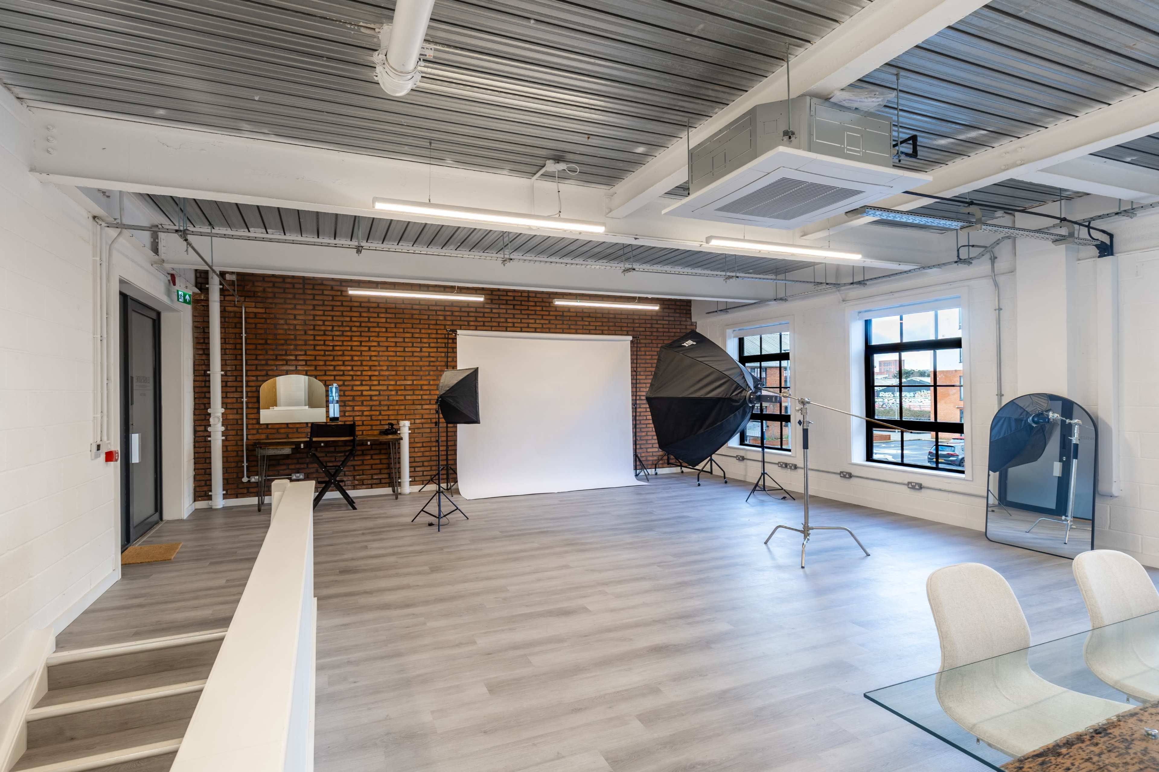 The image shows a spacious, well-lit studio with a brick wall, a large white backdrop, and two softbox lights set up on stands.