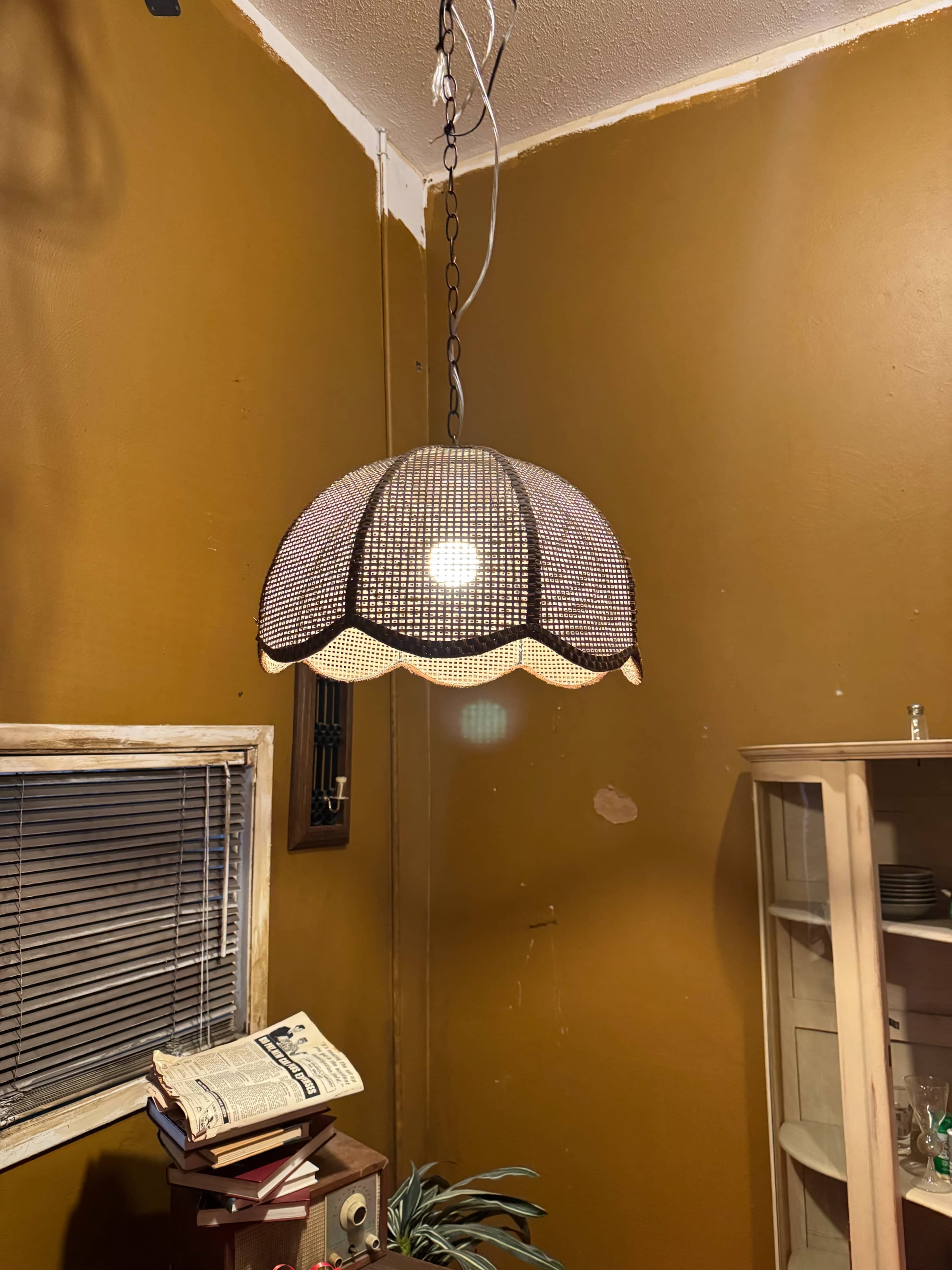 A woven pendant lamp hangs from the ceiling in a room with brown walls and a wooden bookshelf nearby.