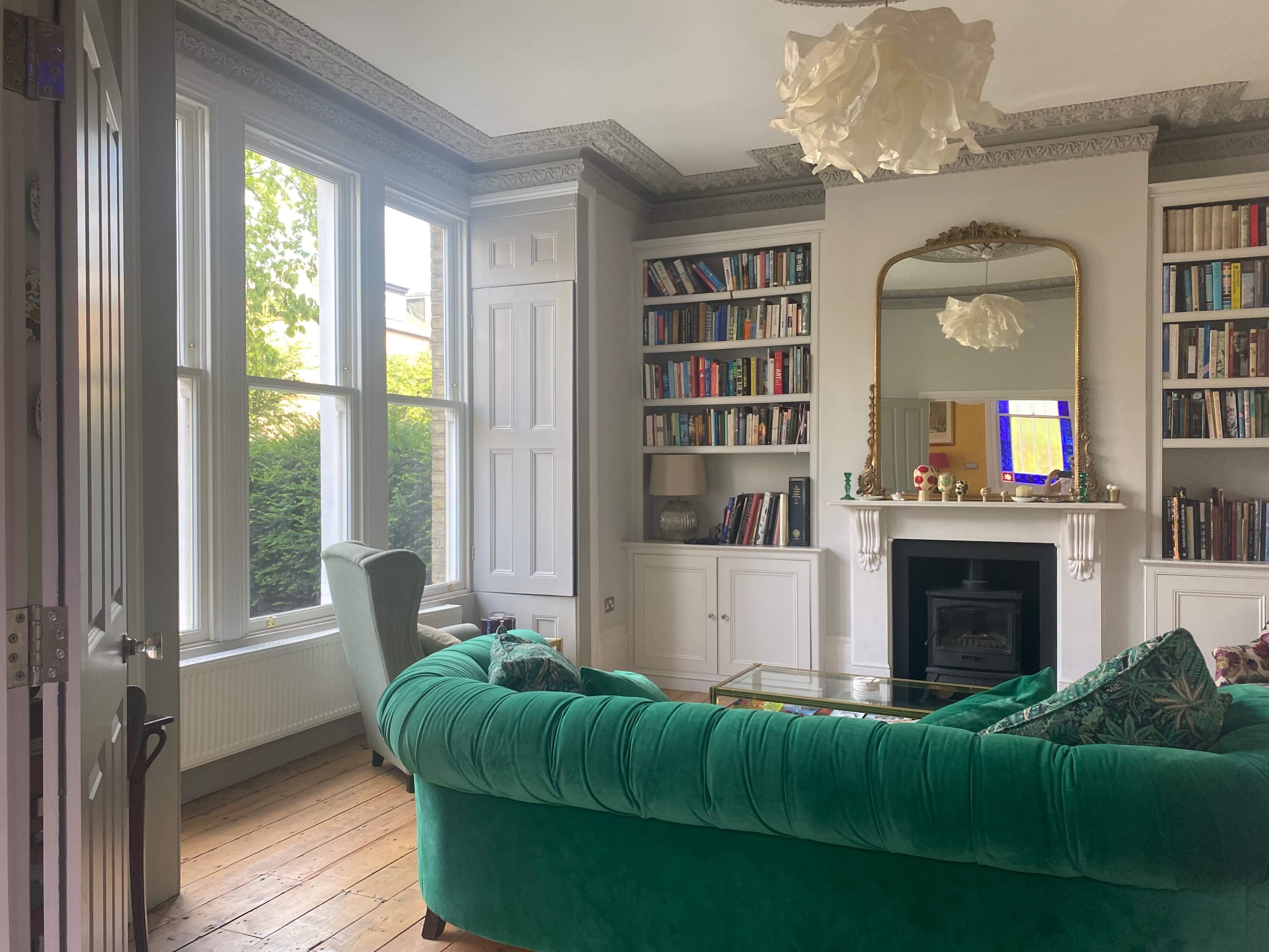 A living room with a green sofa, bookshelves filled with books, a fireplace, and large windows allowing natural light.