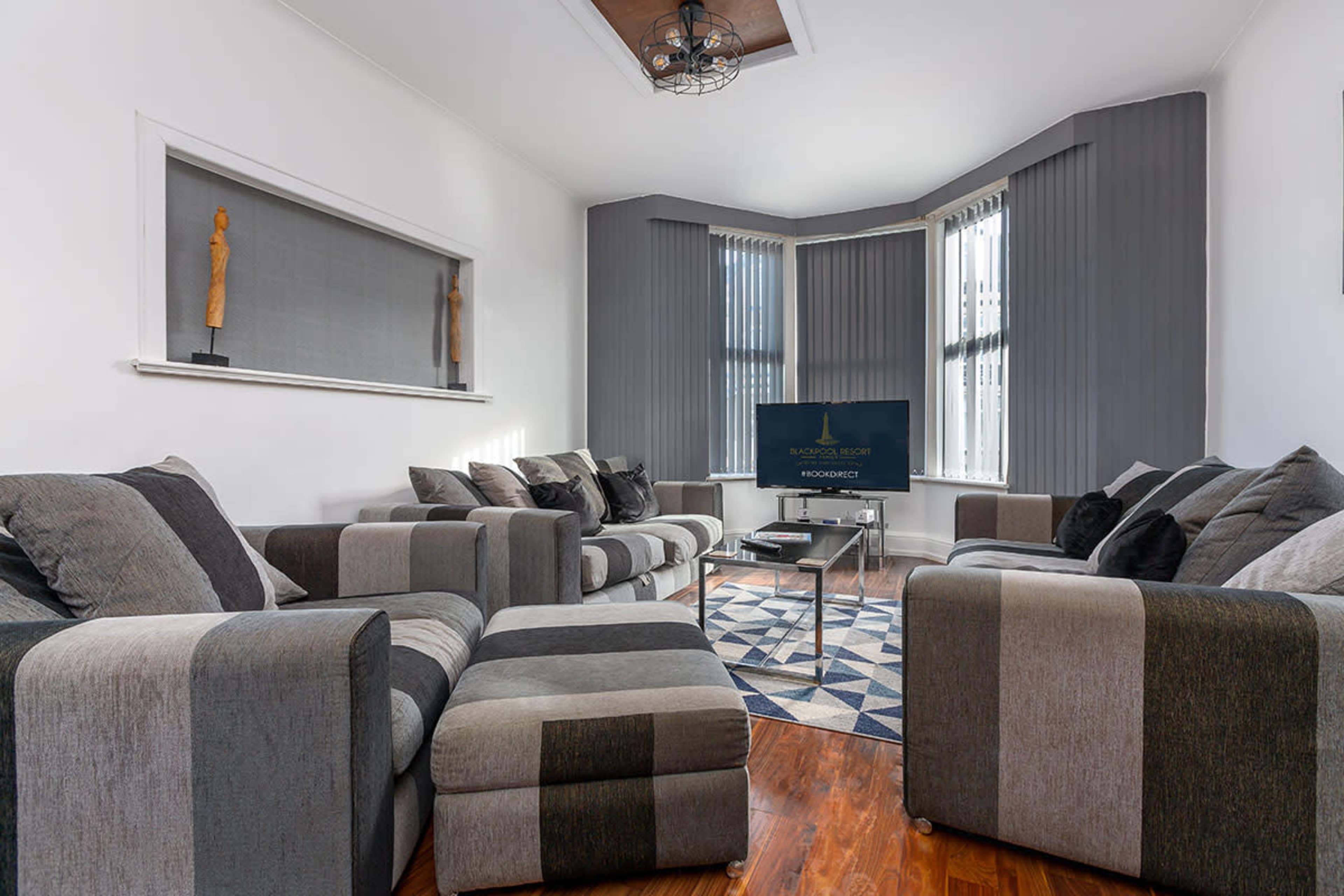 A modern living room with gray striped sofas, a coffee table, and large windows draped with gray curtains.
