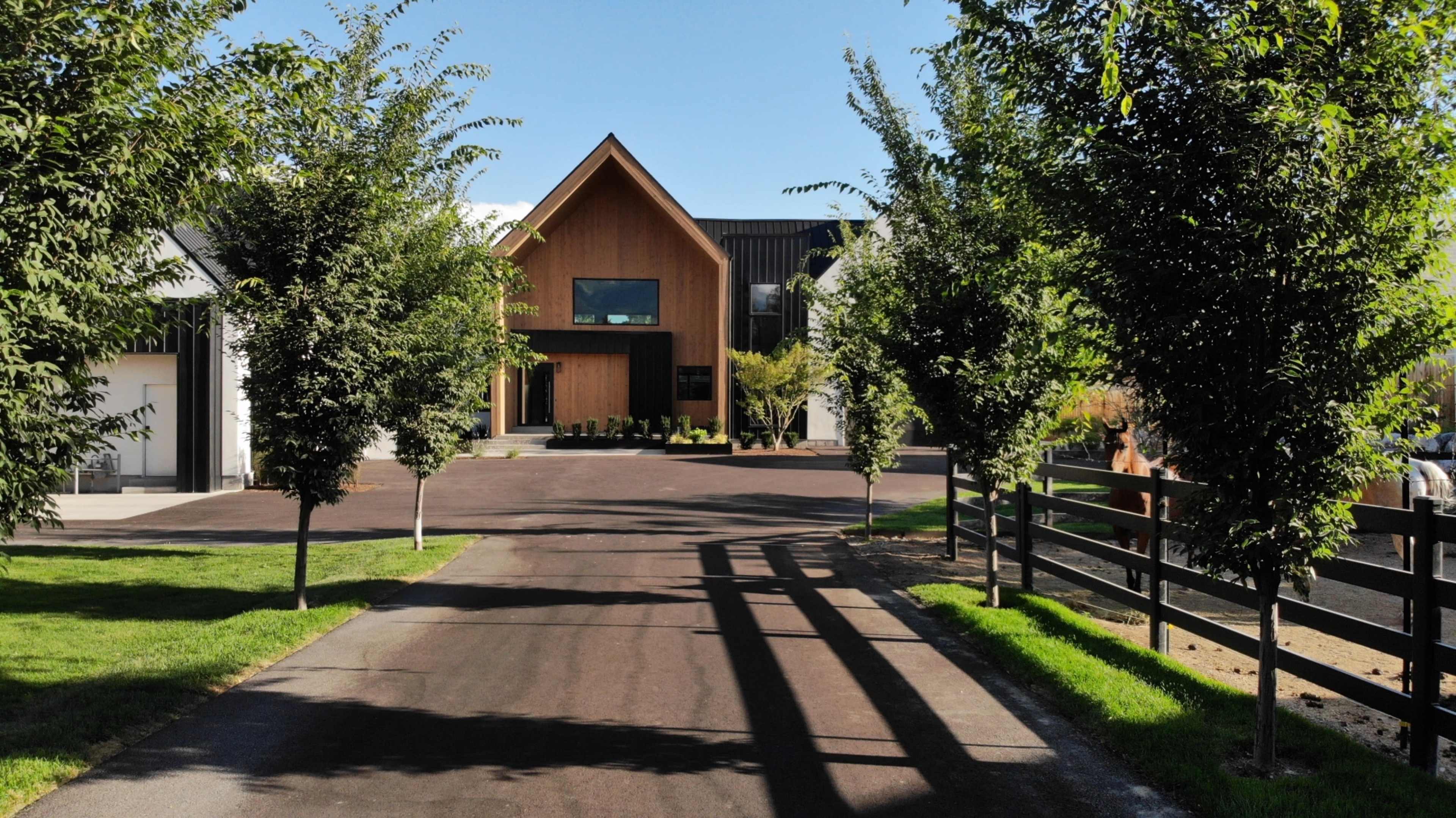A modern house with a wooden facade situated at the end of a tree-lined driveway.