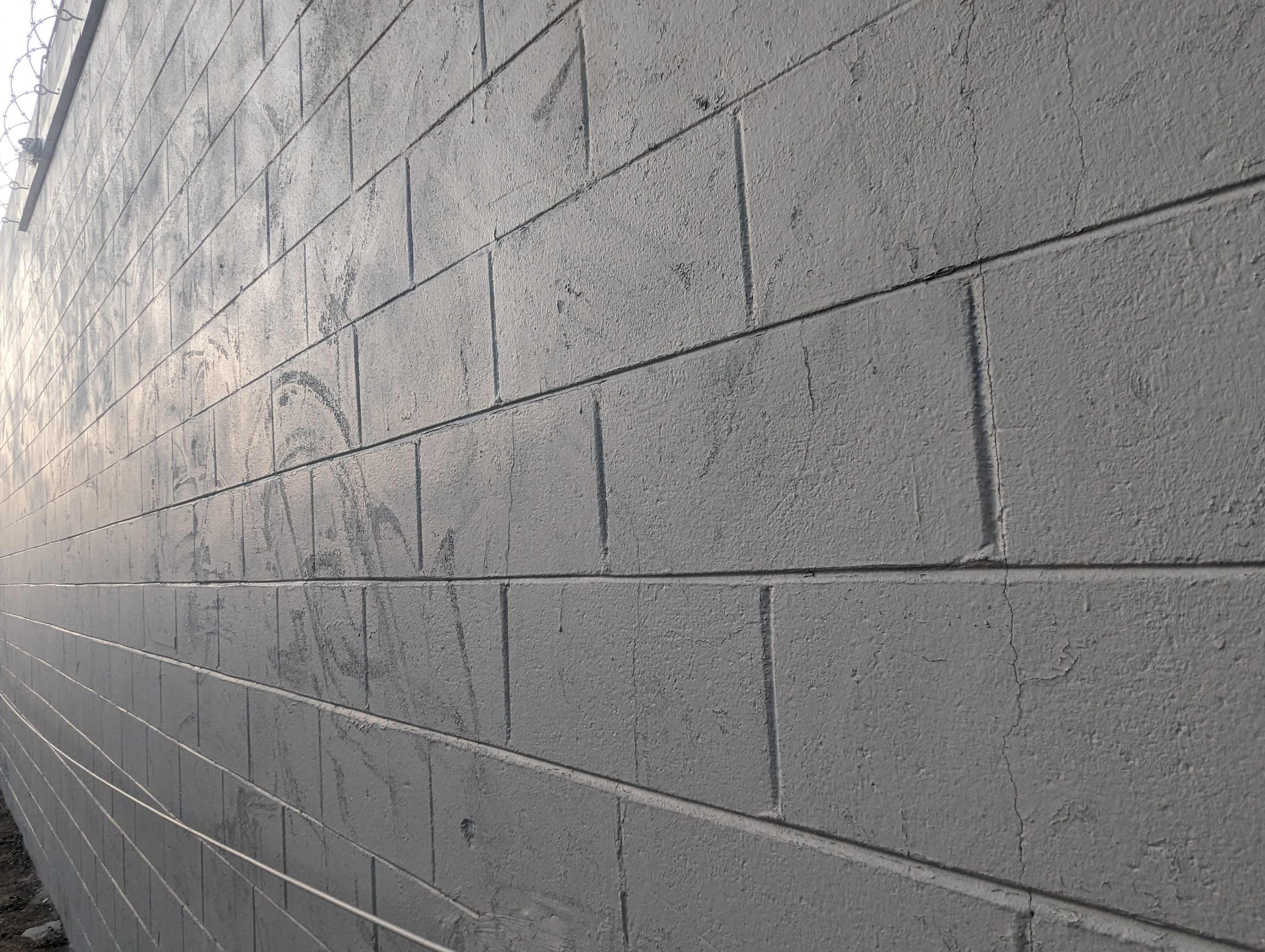 A textured gray concrete wall with visible block patterns and faint markings.
