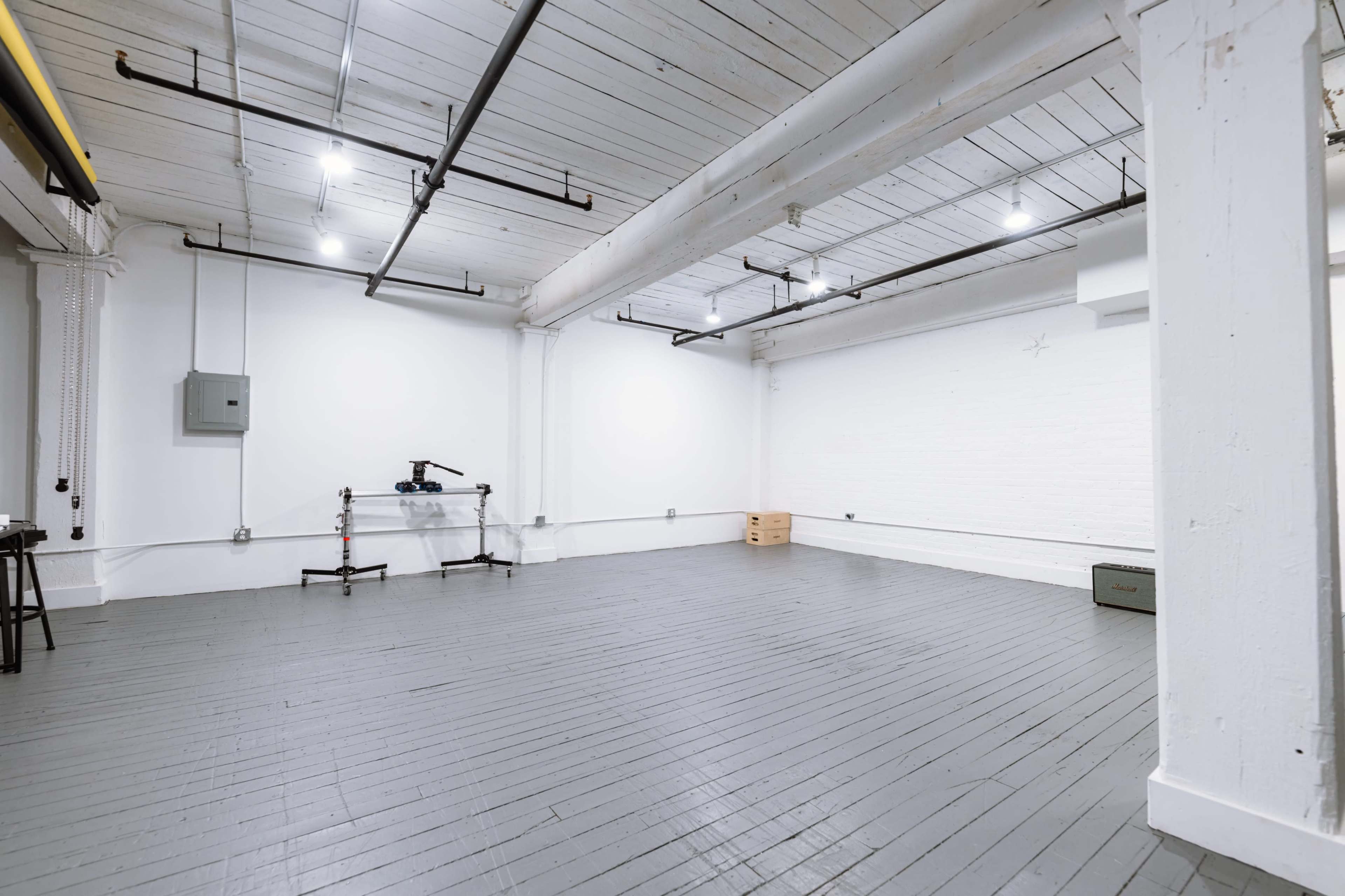The image shows a spacious, empty industrial room with white walls, wooden floors, and exposed beams.