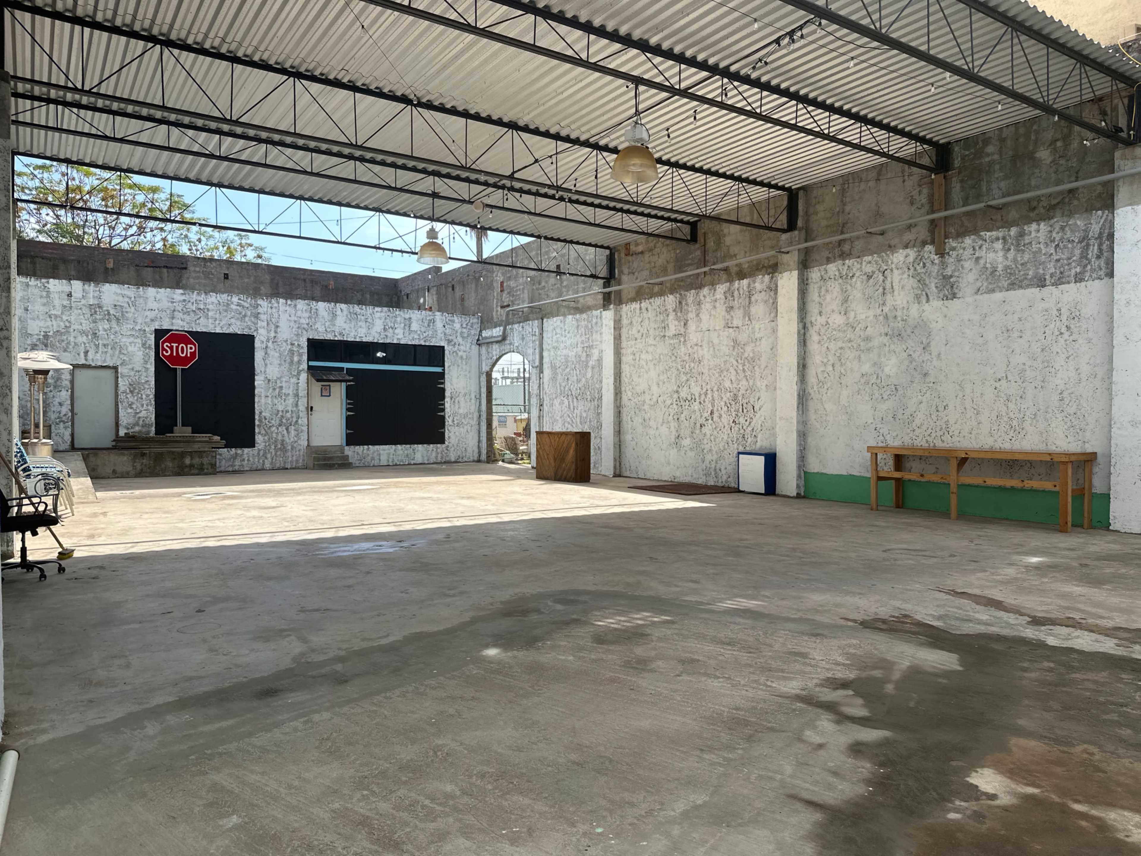 The image shows a large, empty indoor space with concrete floors and walls, featuring a stop sign on one wall and a few scattered items, including a table.