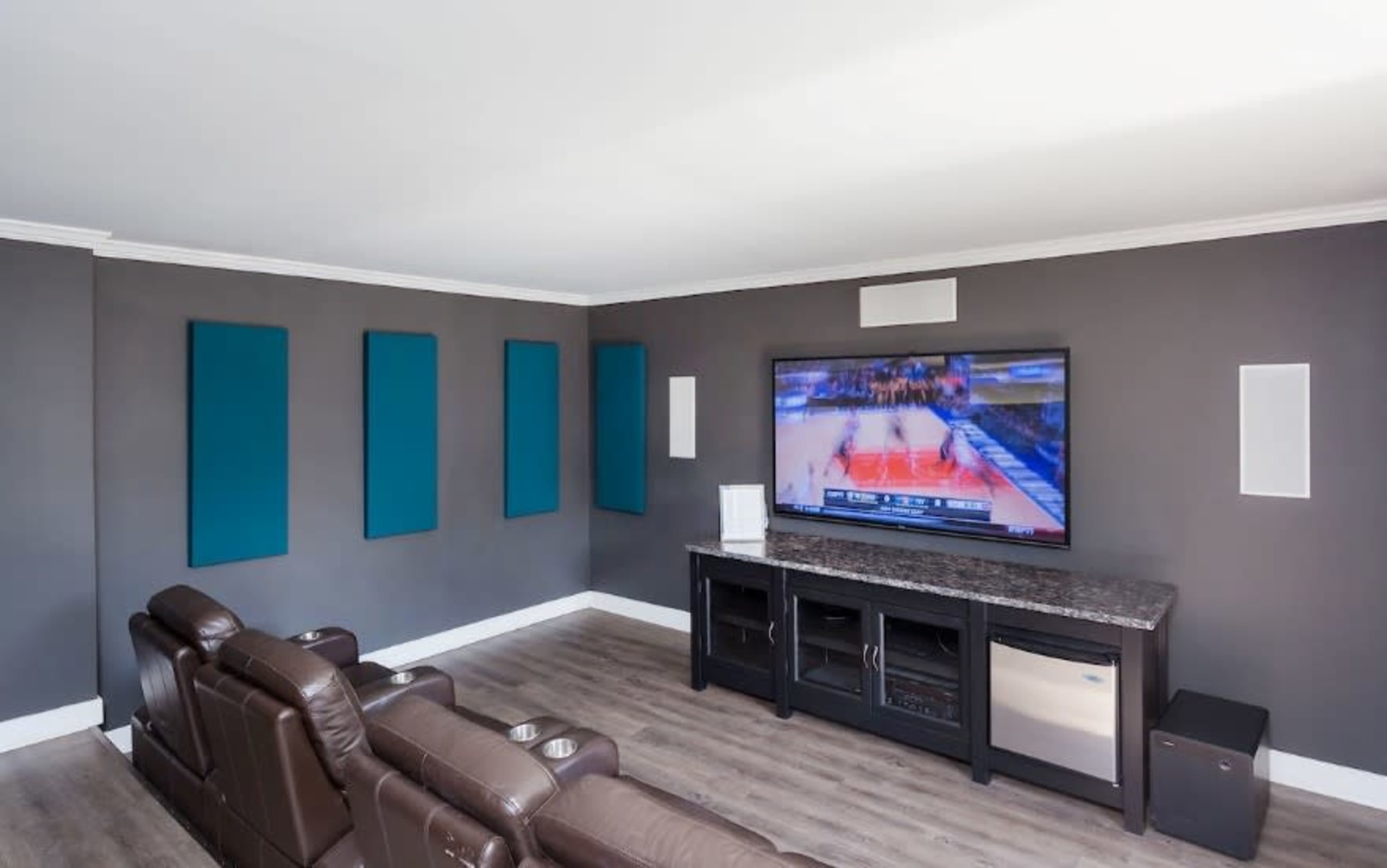 A modern living room features leather recliners facing a large flat-screen television mounted on a gray wall.