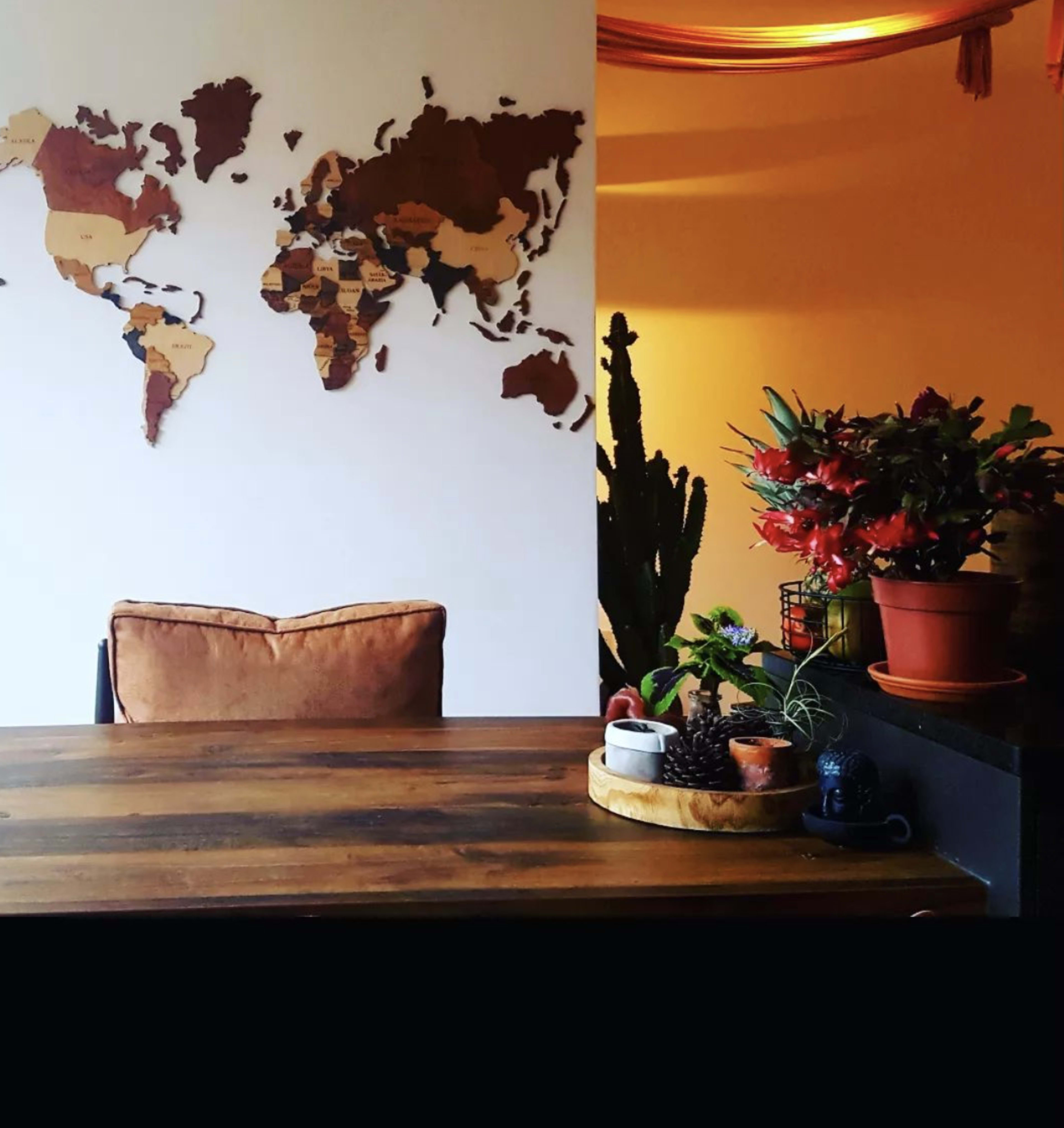 A wooden table with a map of the world made from various materials mounted on the wall, alongside potted plants and decorative items.