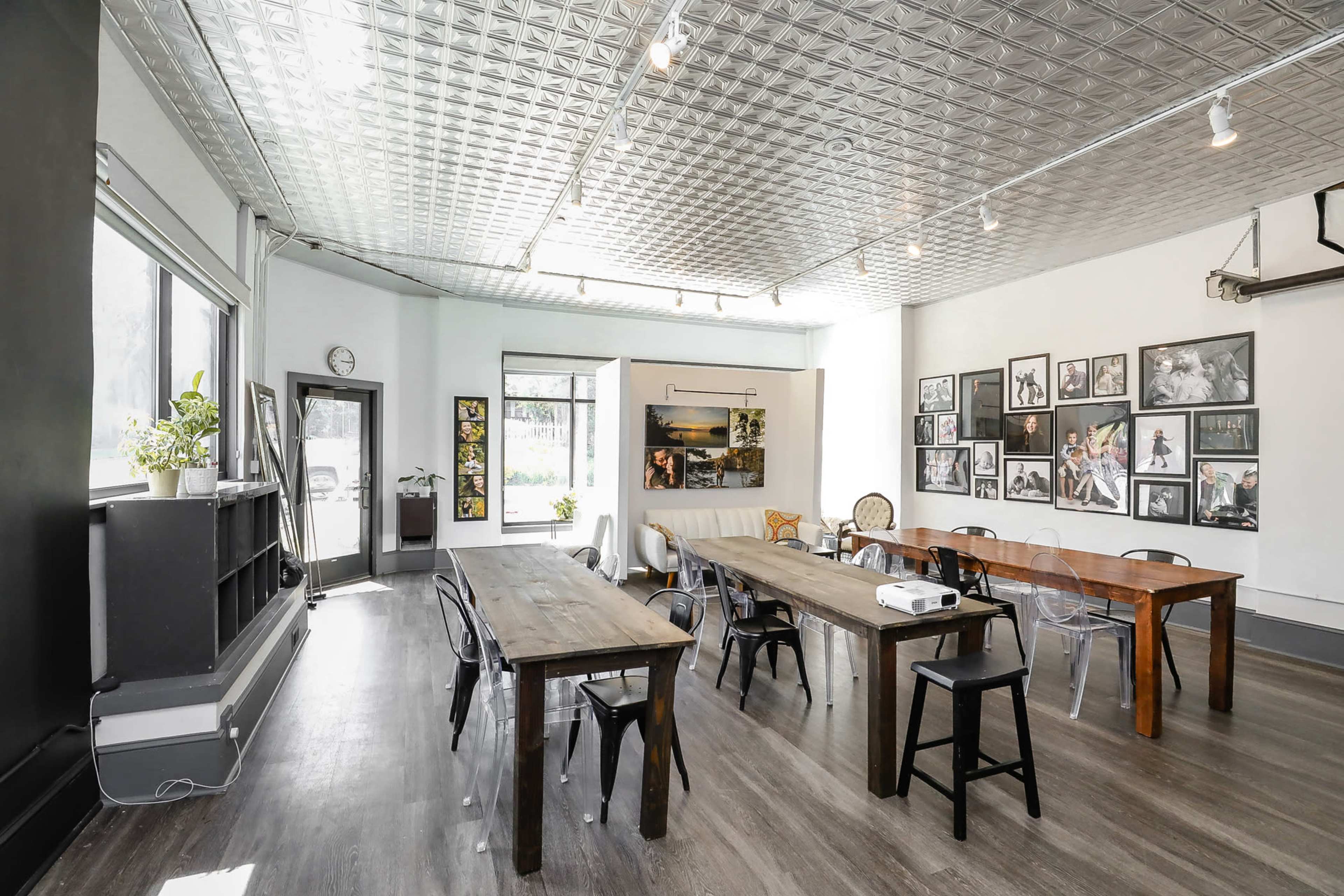 A bright, modern workspace with several wooden tables, a comfortable seating area, and a wall adorned with various framed photographs.