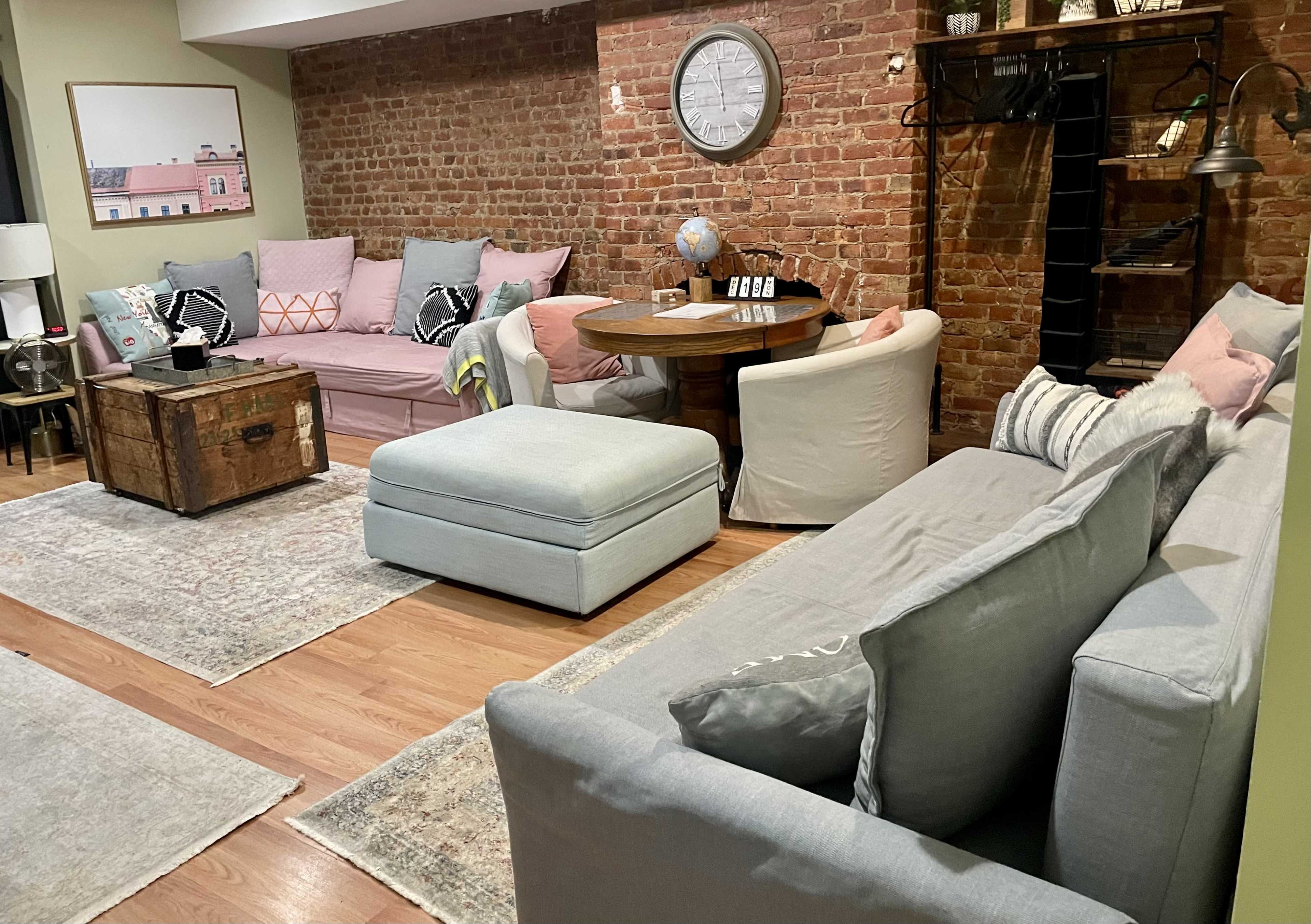 A cozy living room with exposed brick walls, two sofas, a round dining table, and a vintage trunk as a coffee table.