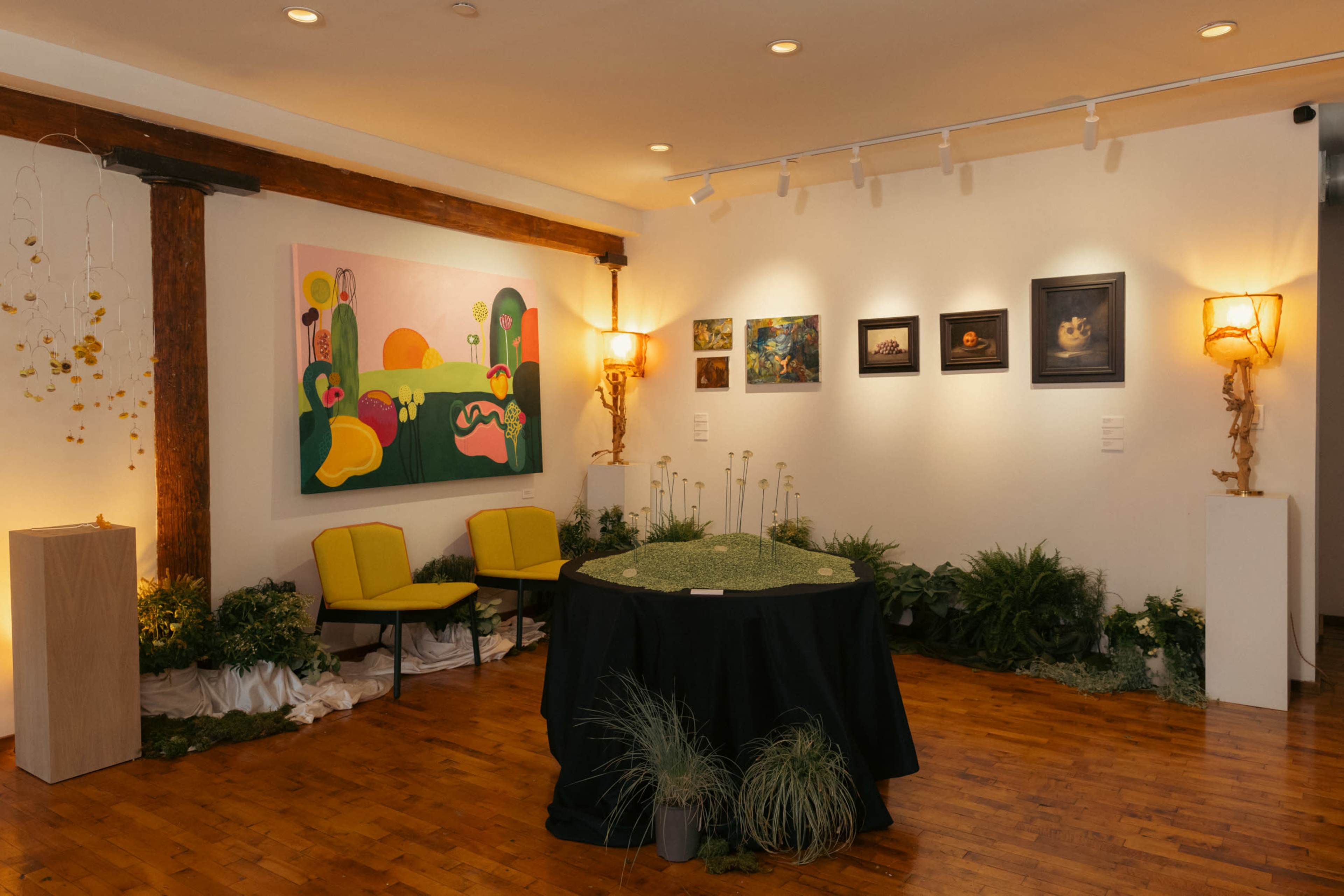 The scene features an art gallery with a colorful abstract painting on the wall, surrounded by various framed artworks, green seating, and decorative plants throughout the space.