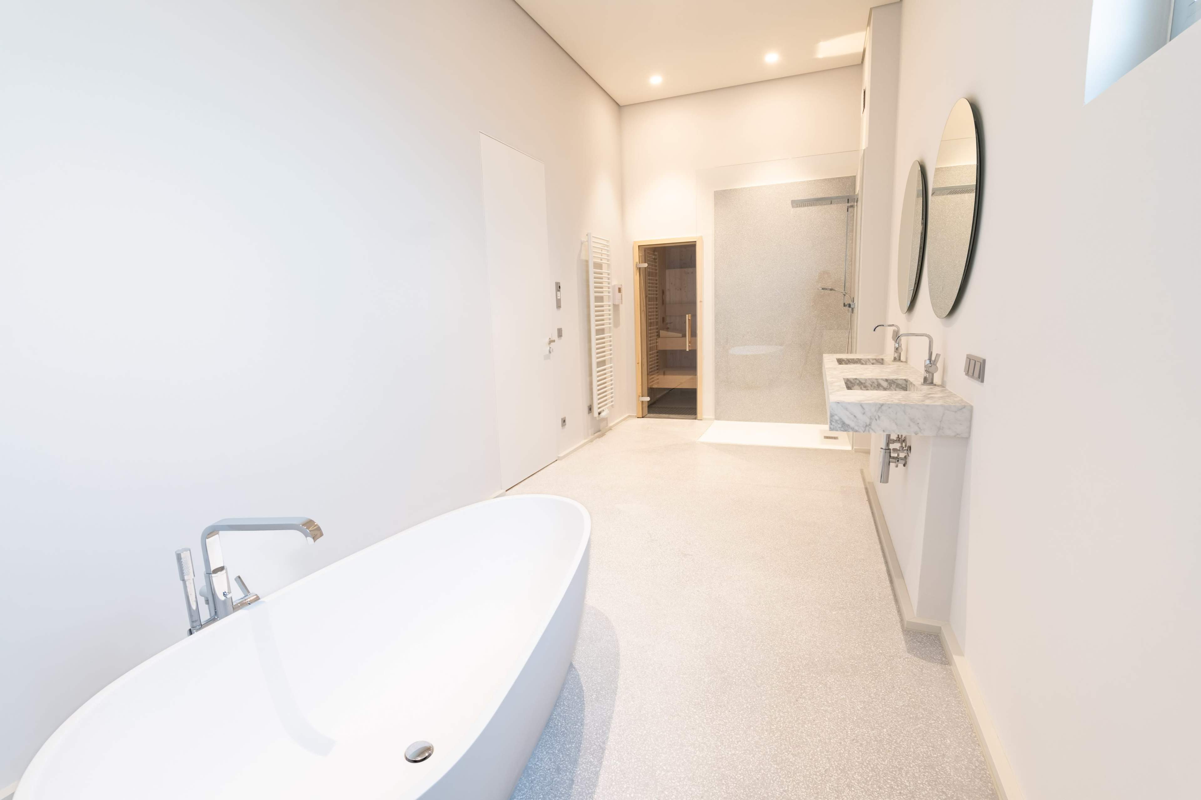 The image shows a modern, spacious bathroom featuring a freestanding bathtub, dual sinks with a marble countertop, and a walk-in shower.