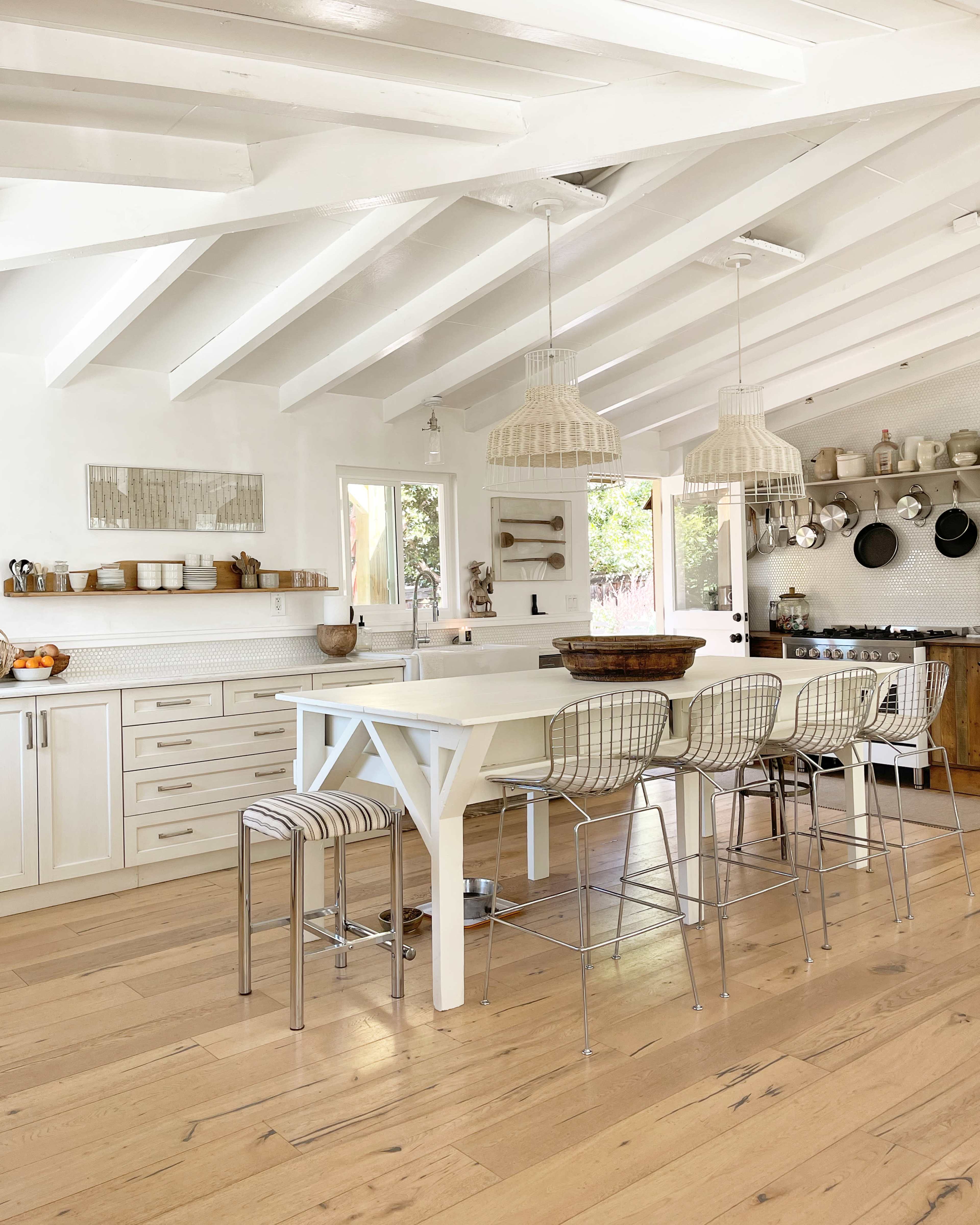 A bright kitchen features white cabinets, a large island with bar stools, and hanging light fixtures.