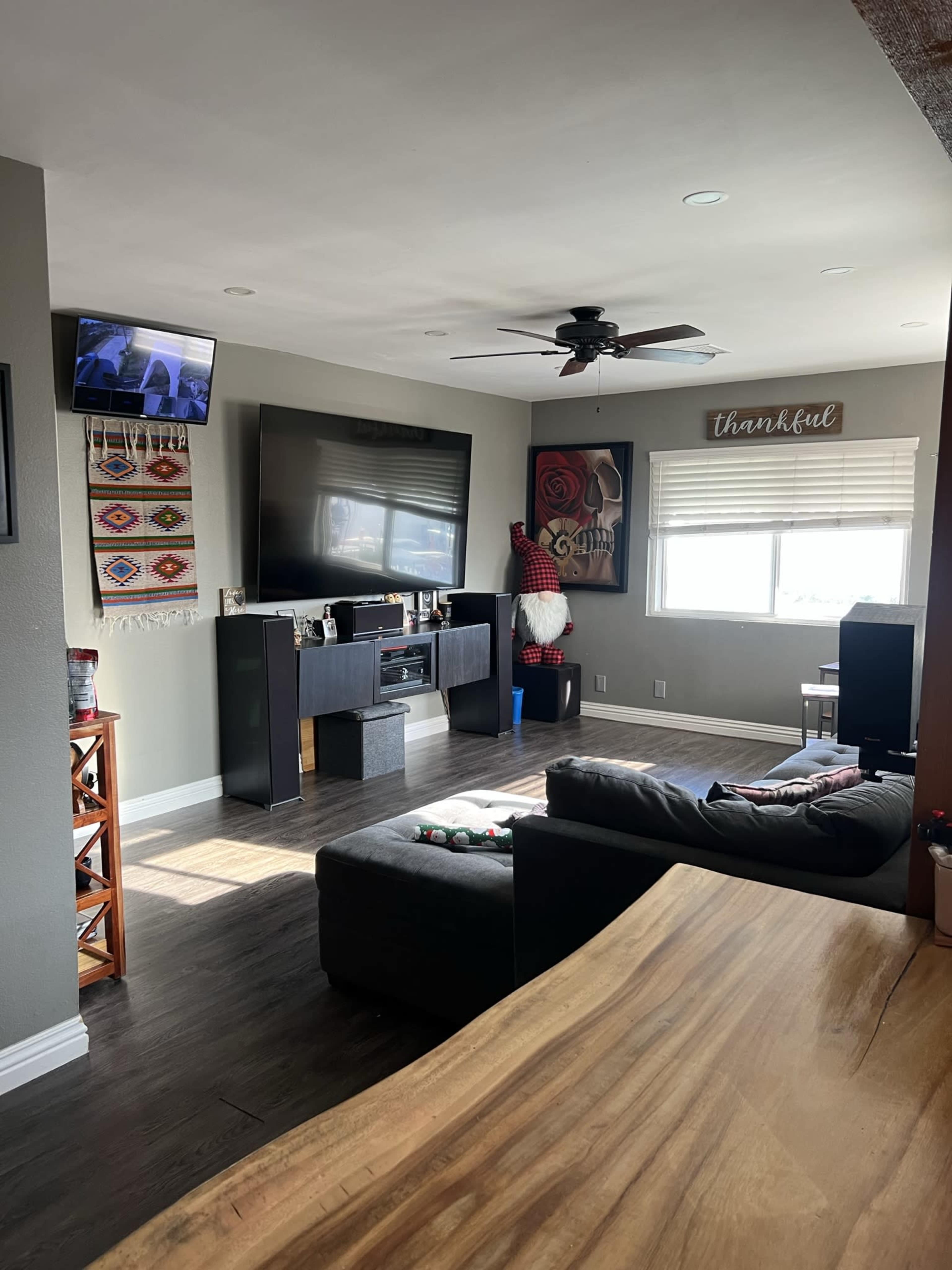A living room featuring a large television, a black couch, and decorative wall art, with a window allowing natural light to enter the space.