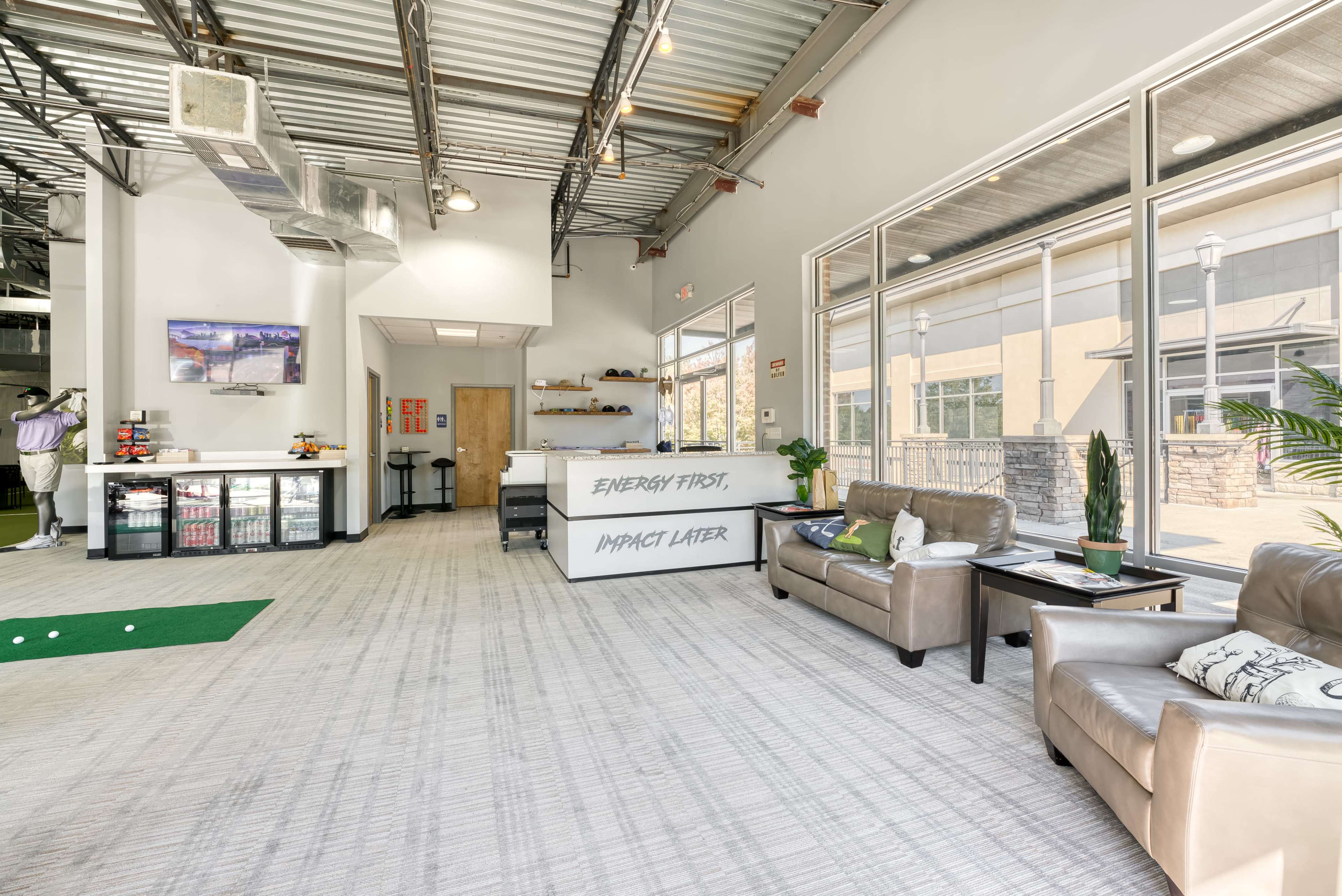 A modern indoor space with a seating area, a reception desk displaying a motivational message, and large windows providing natural light.