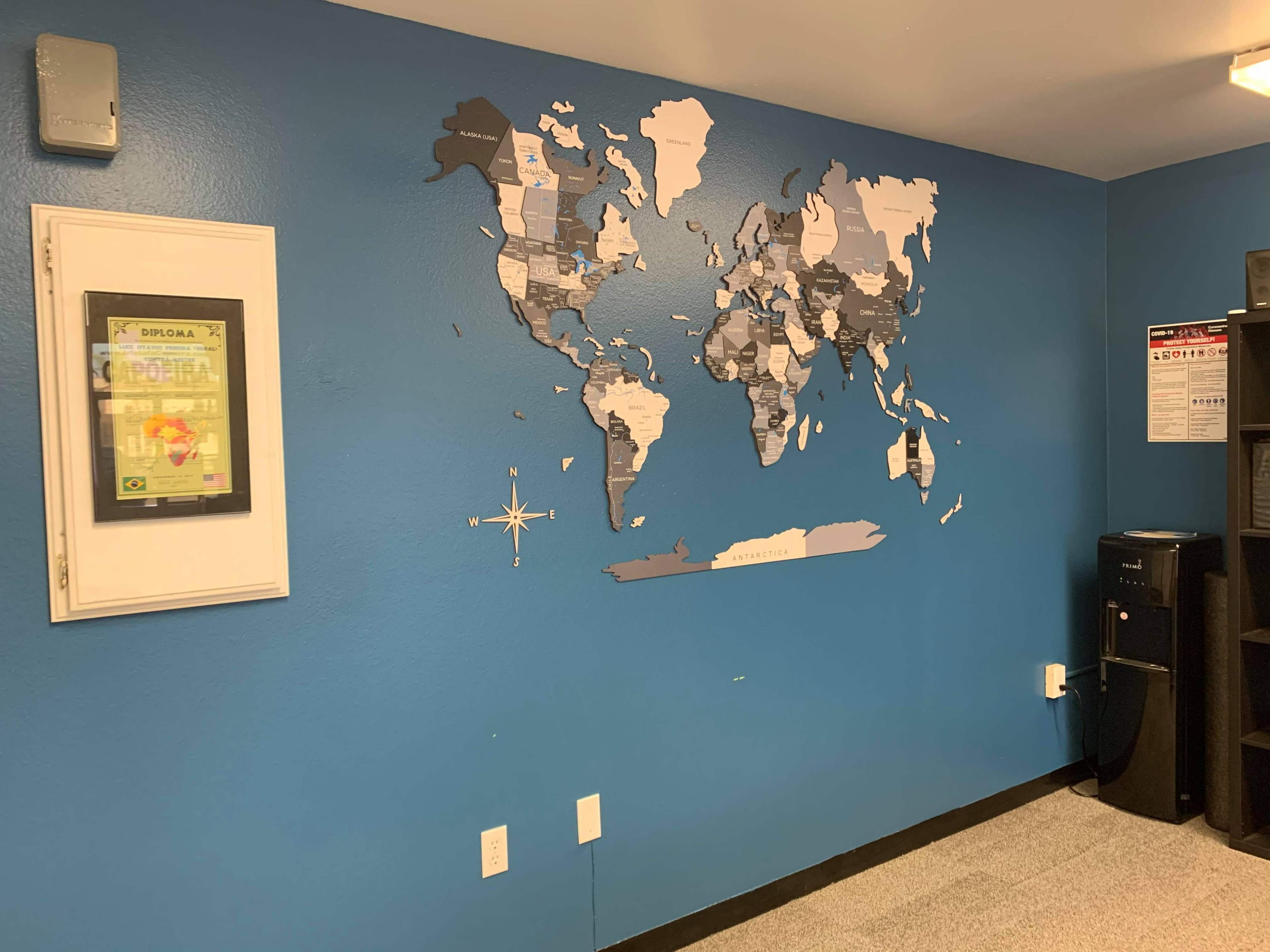 A blue wall with a world map mural and a framed diploma on the left side.