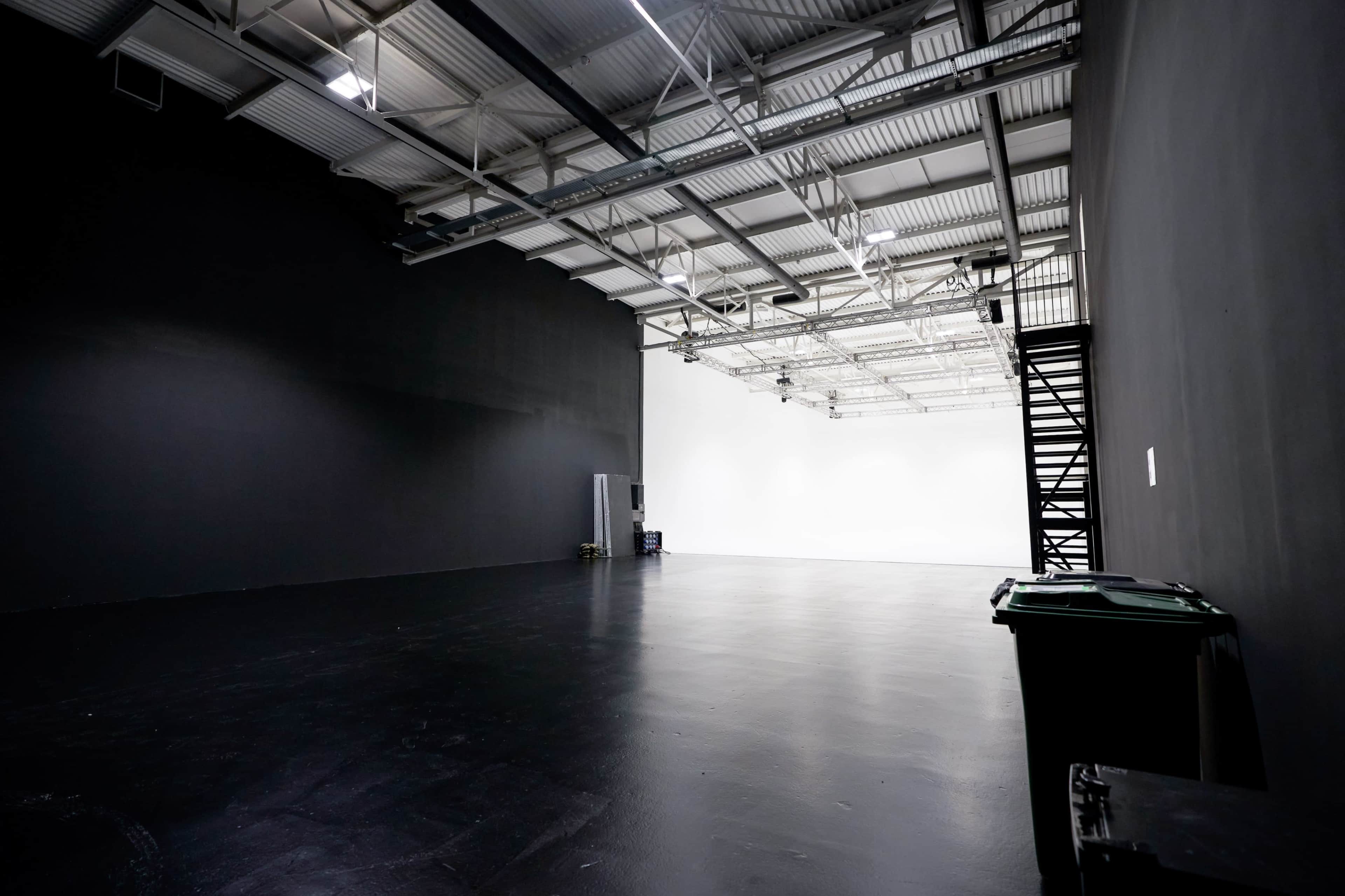The image shows a spacious studio with a black wall on one side and a white wall on the opposite side, featuring a polished floor and minimal furnishings.