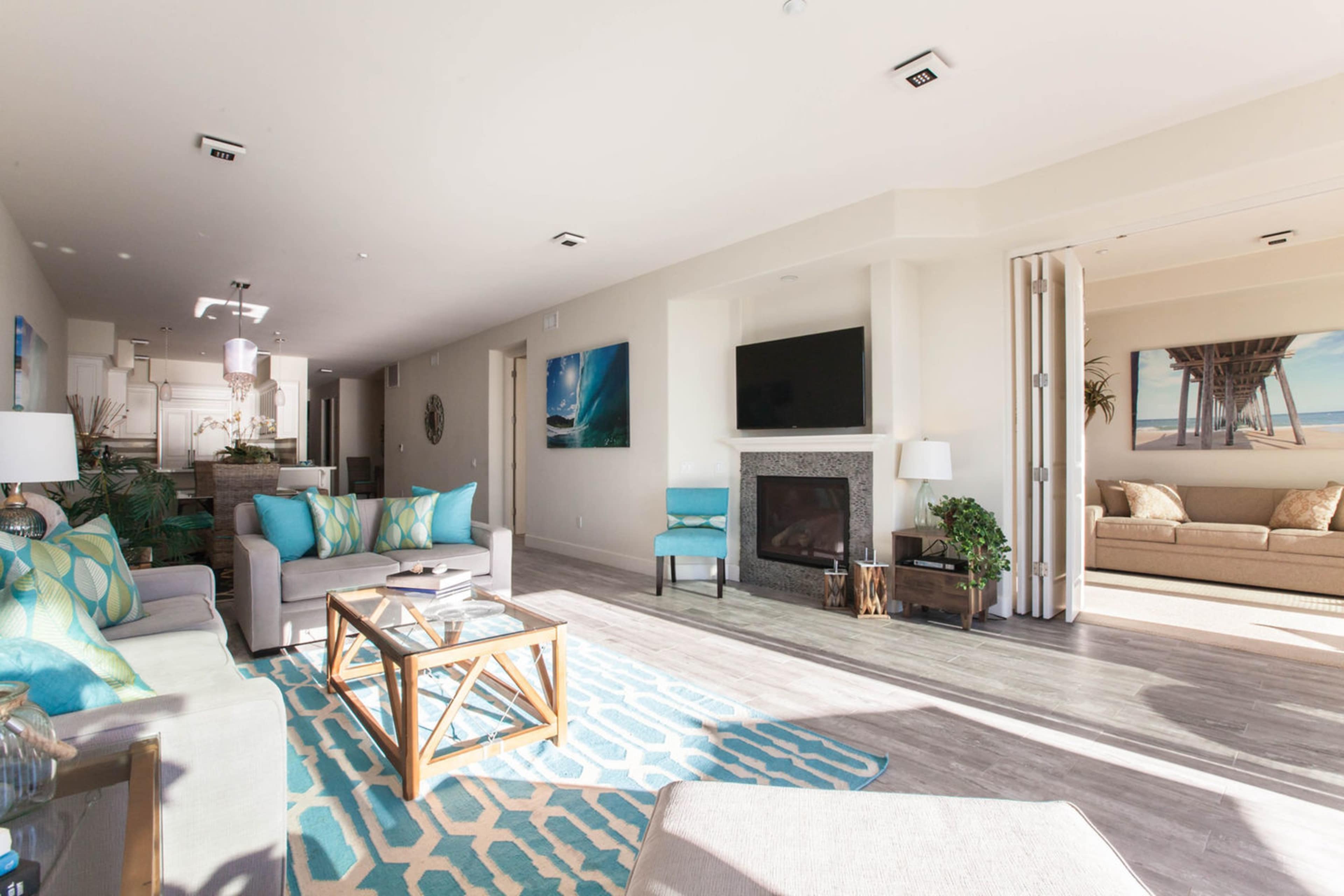 A bright living room features a fireplace, comfortable seating, and large windows that open to a view of a nearby area.