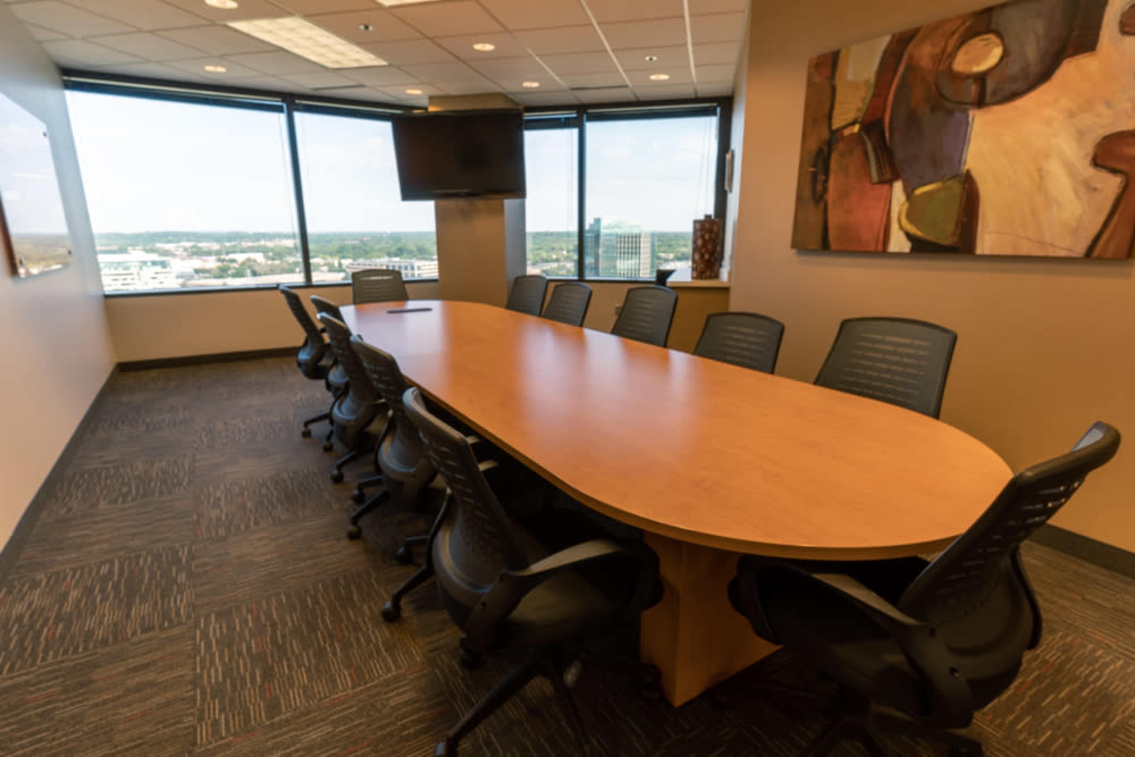 The image shows a modern conference room featuring a long wooden table surrounded by black office chairs, with large windows providing an expansive view.