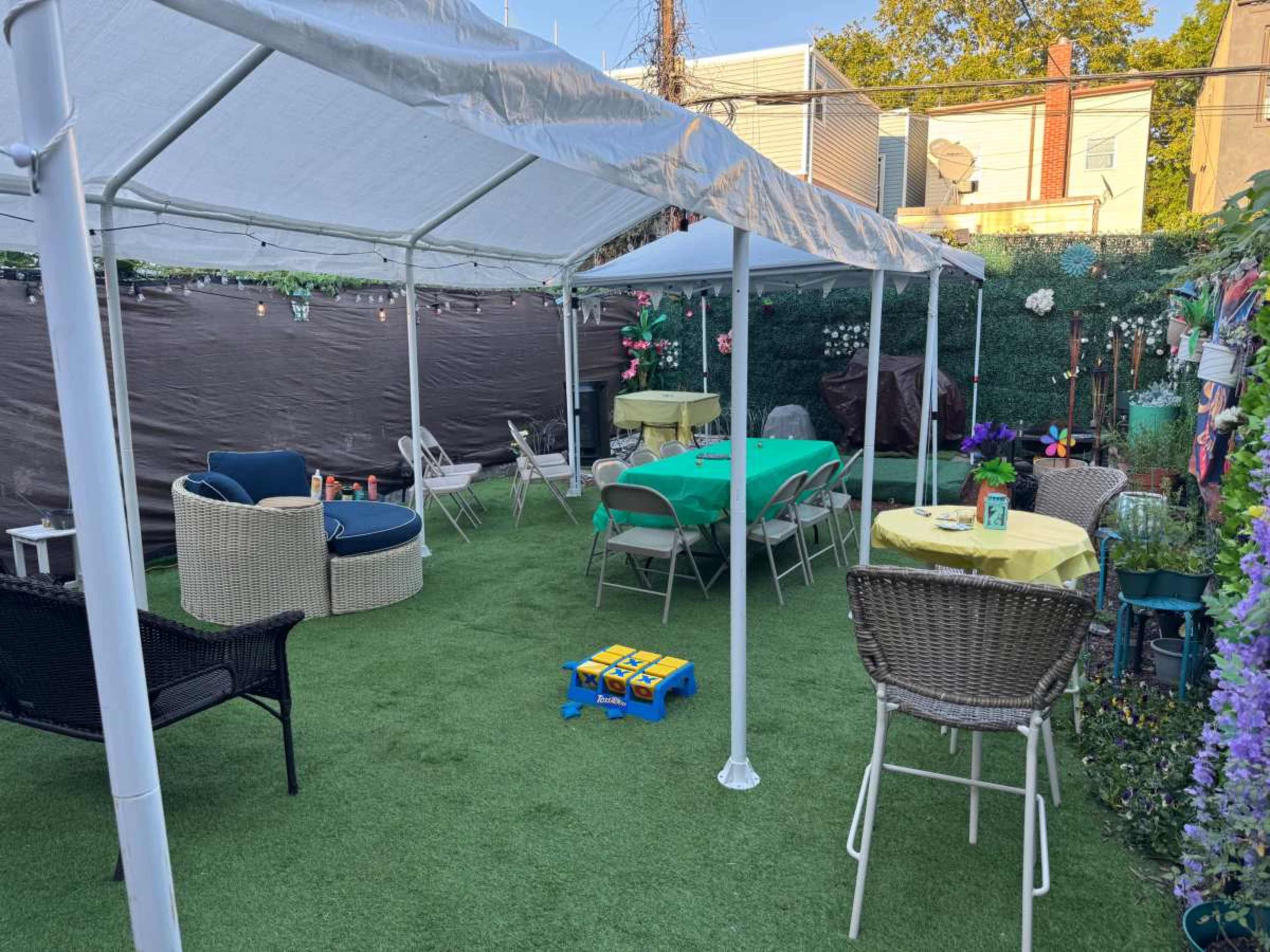 The image shows a tented outdoor area with green grass-like flooring, multiple tables covered in bright tablecloths, and various seating arrangements.