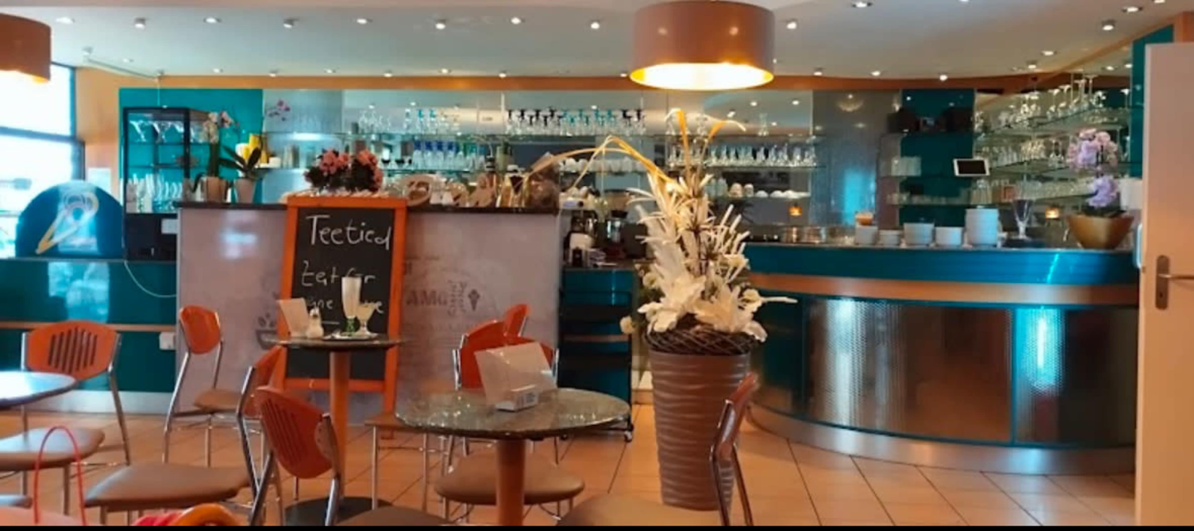 The image shows a modern café interior with colorful decor, tables, and a counter displaying various drinks and glassware.