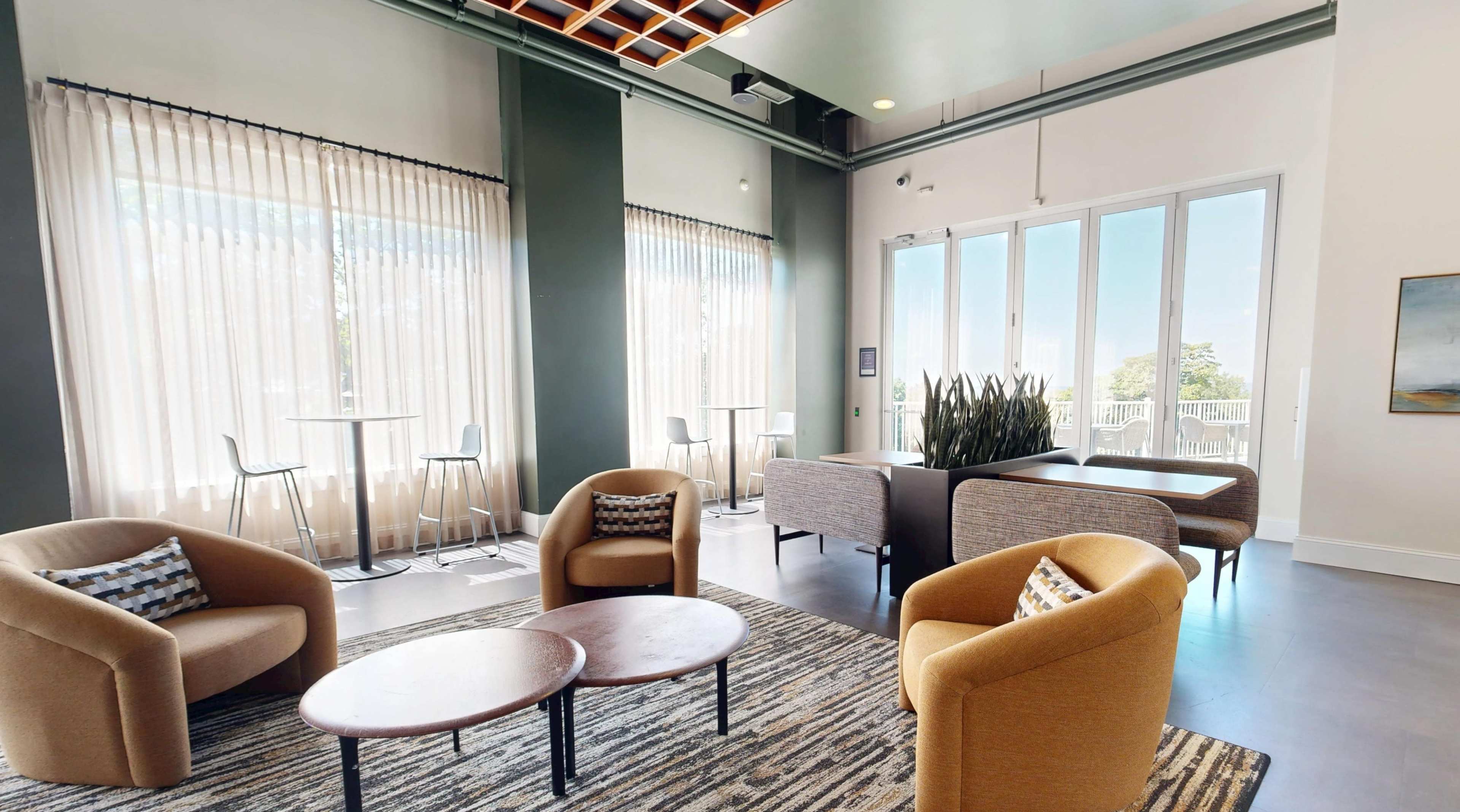 The image shows a modern lounge area with four armchairs, two round coffee tables, and large windows letting in natural light.