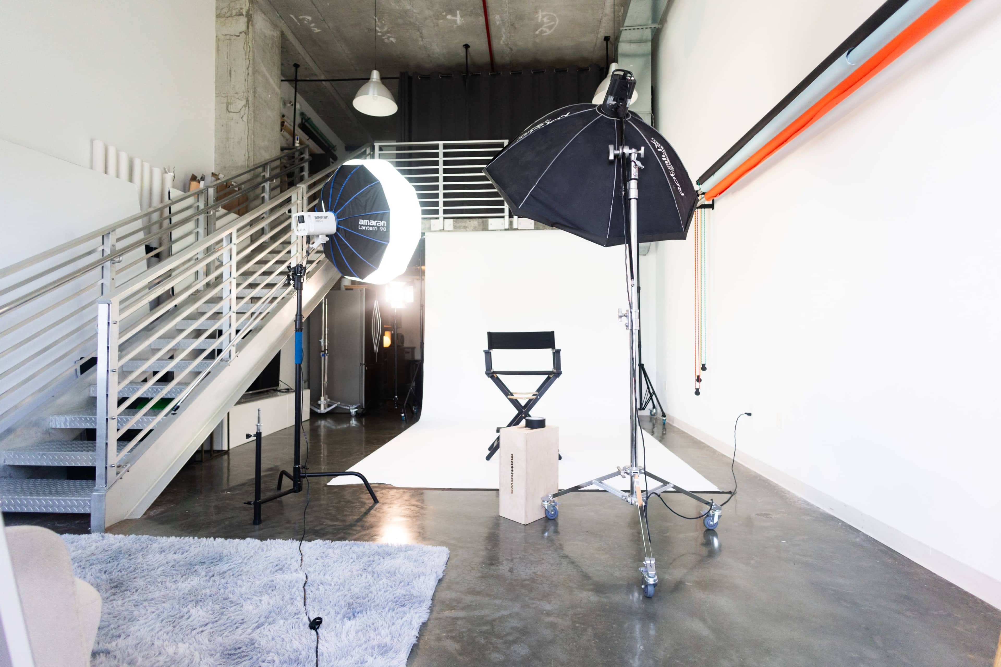 The image shows a well-lit photography studio with a backdrop, a light setup, and a director's chair.