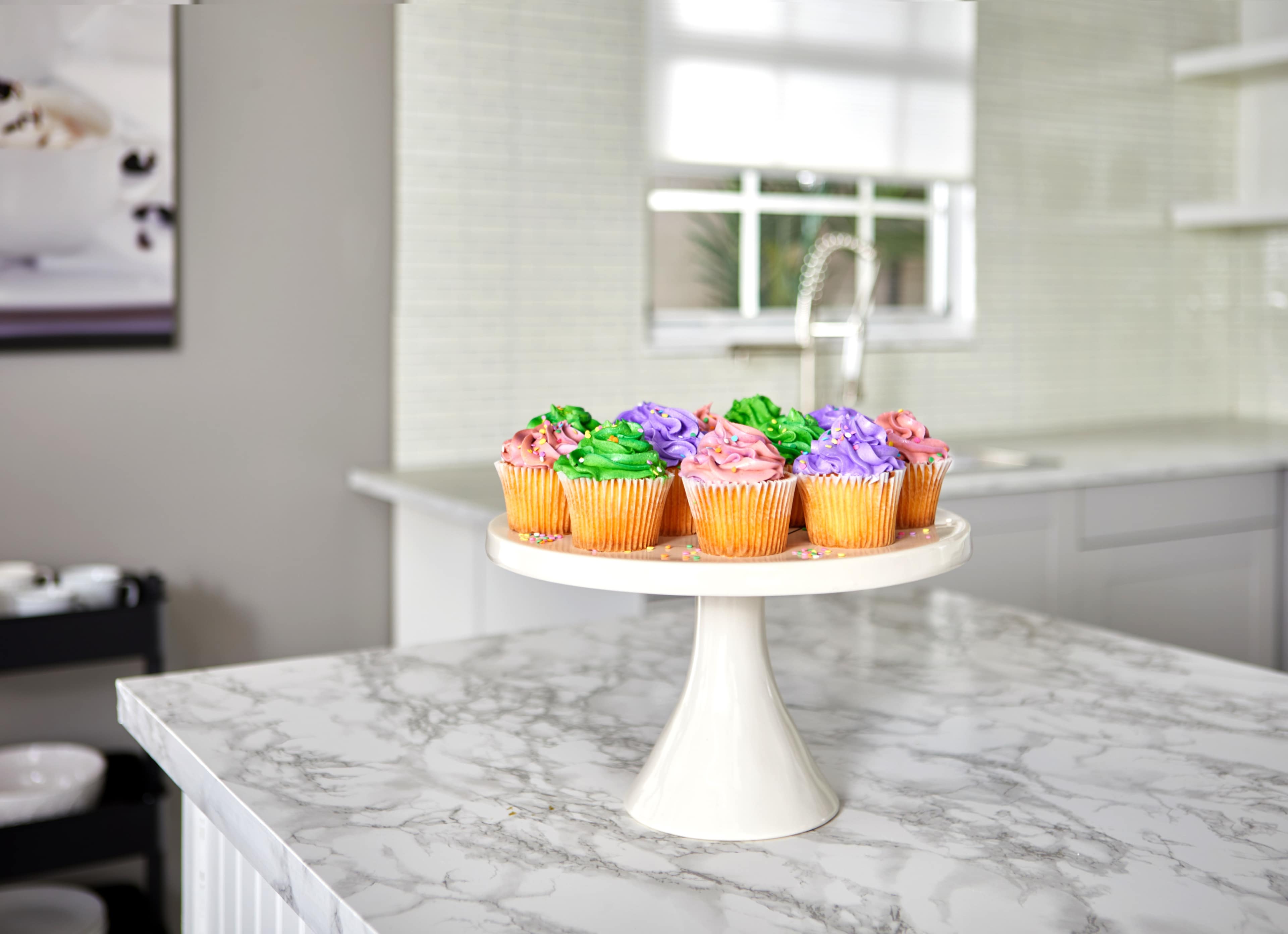 A stand of colorful cupcakes is displayed on a marble kitchen countertop.