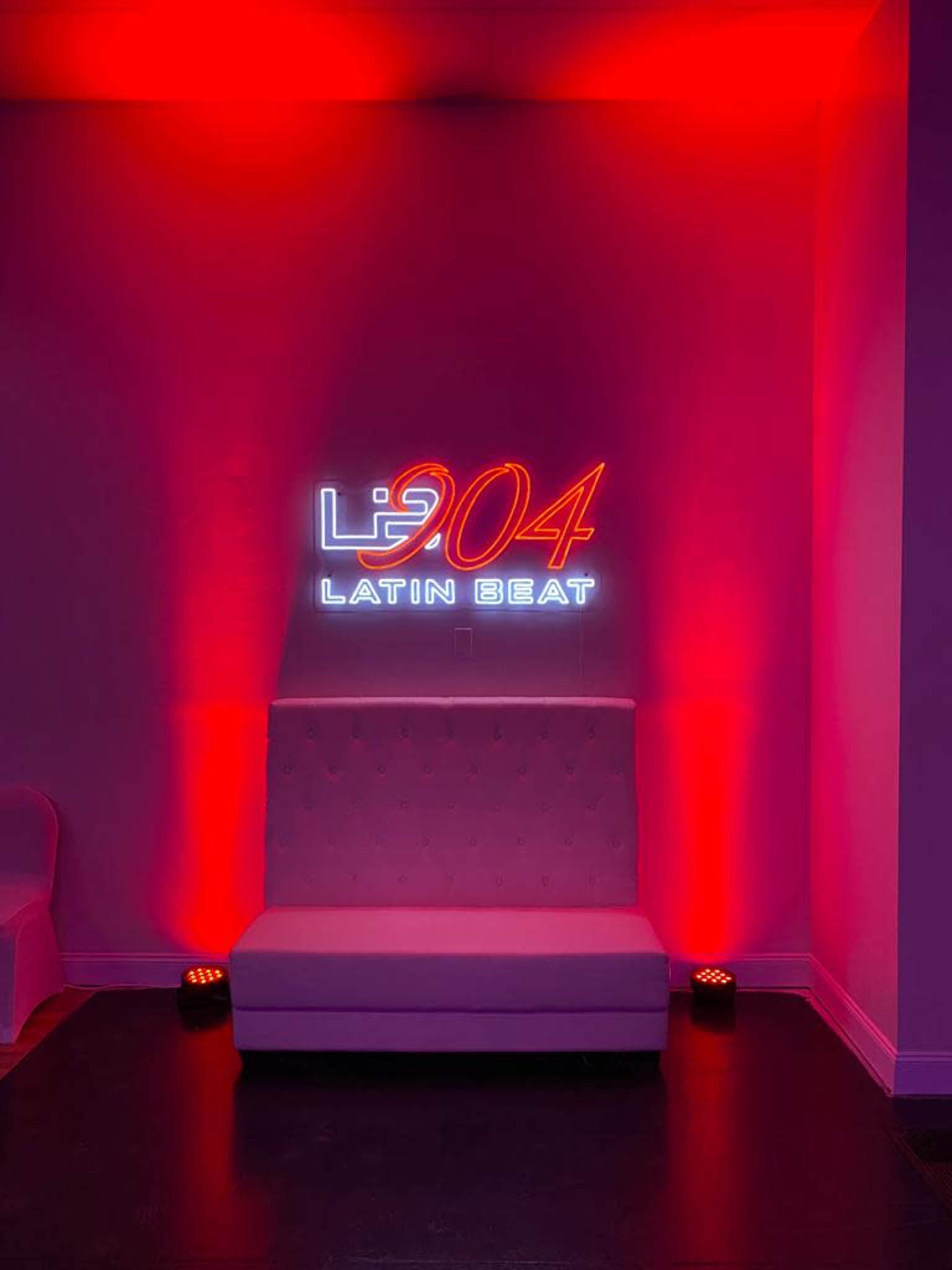 A neon sign reading "904 LATIN BEAT" is displayed on a wall above a white couch, illuminated by red lighting.