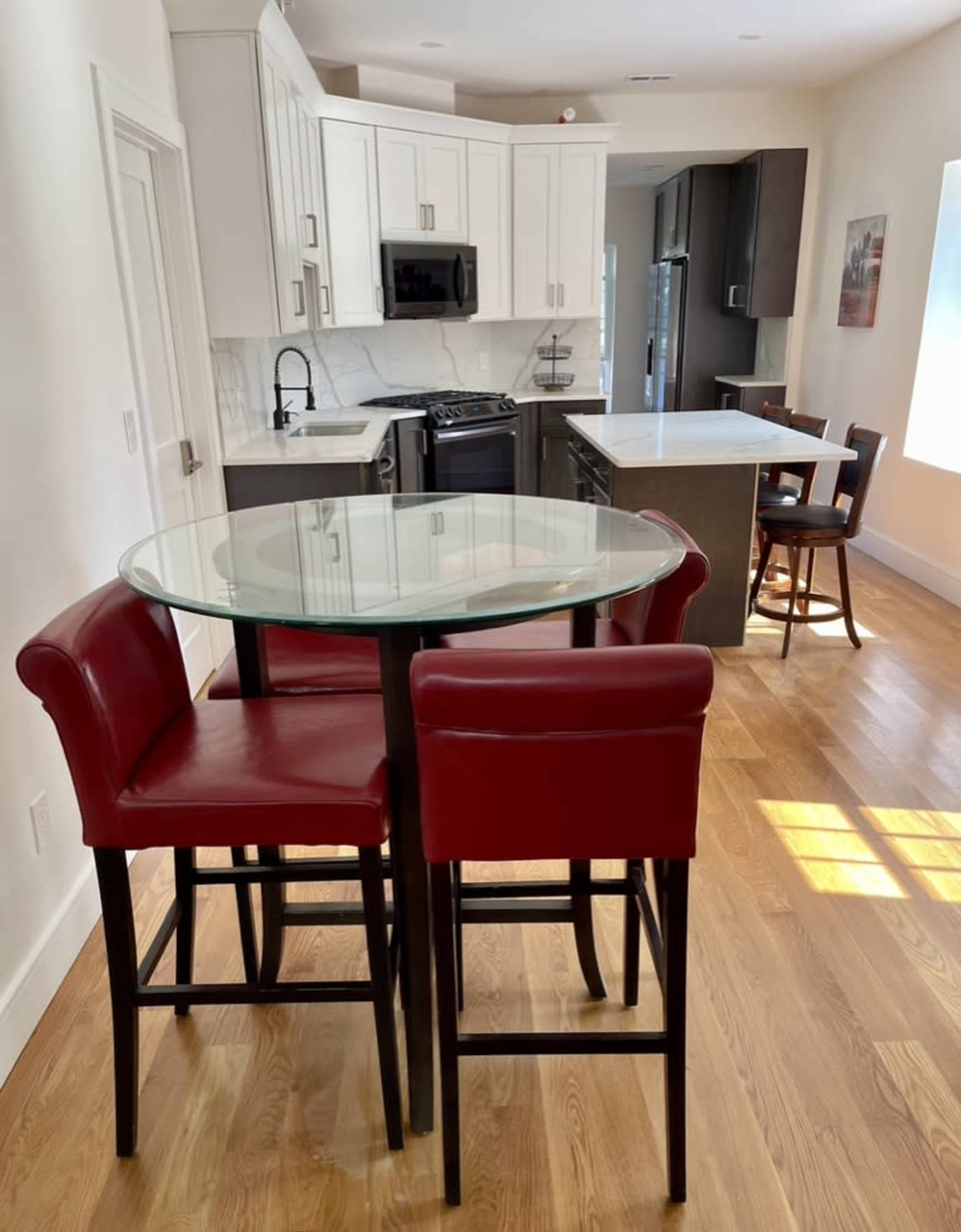 A modern kitchen with a glass-top dining table surrounded by red high-back chairs, along with black and white cabinetry in the background.