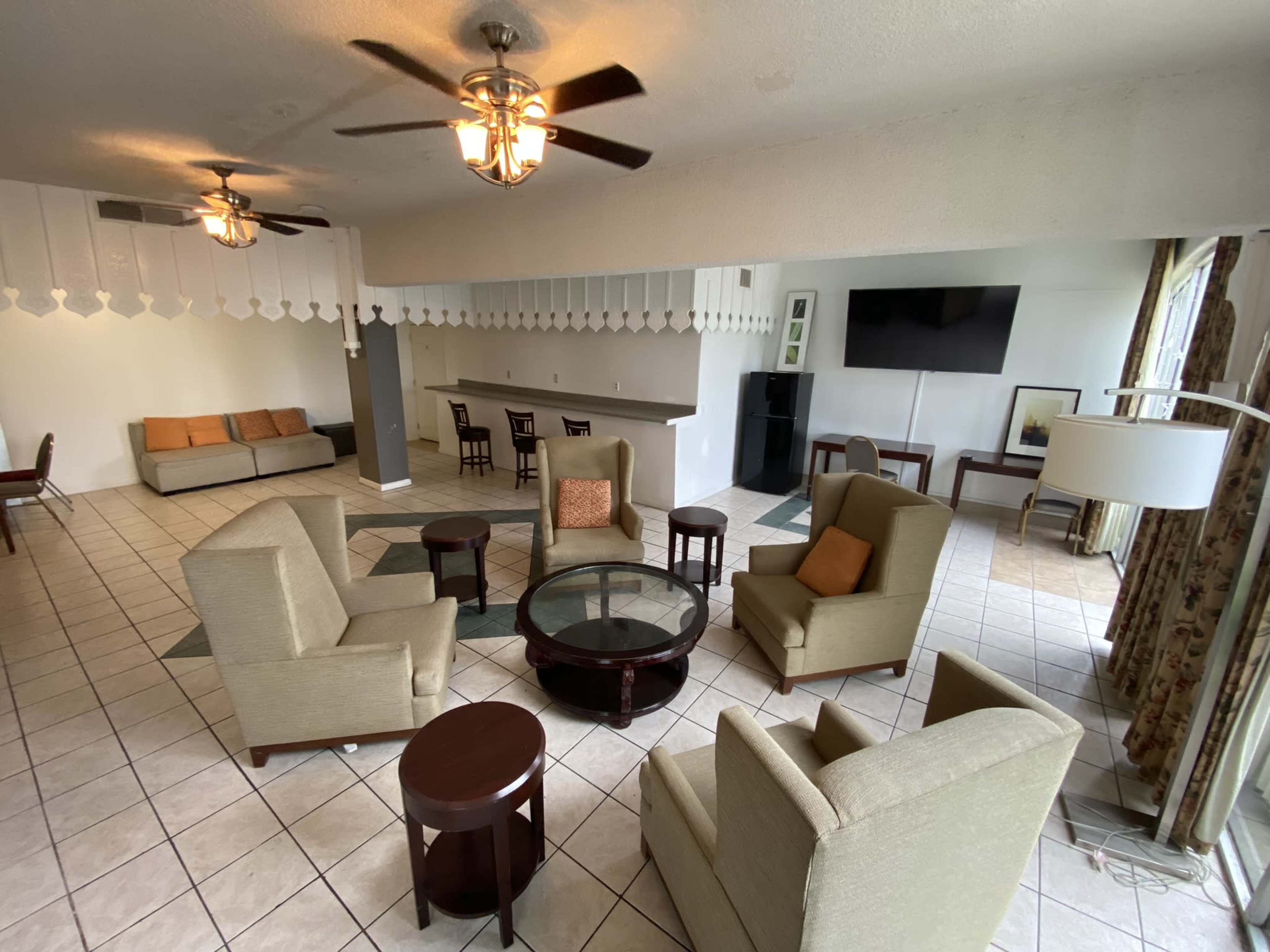 An interior lounge area with several seating arrangements, including chairs and a couch, along with a bar counter and a television mounted on the wall.